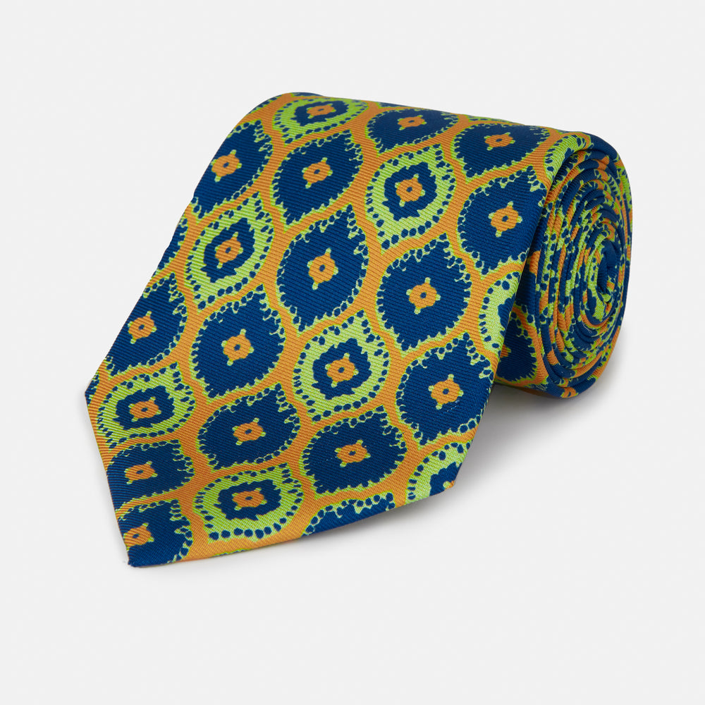 The Yellow Medallion Printed Silk Tie by Turnbull & Asser features a bold abstract medallion pattern in blue, green, and orange on yellow silk, displayed rolled up against a plain white background.