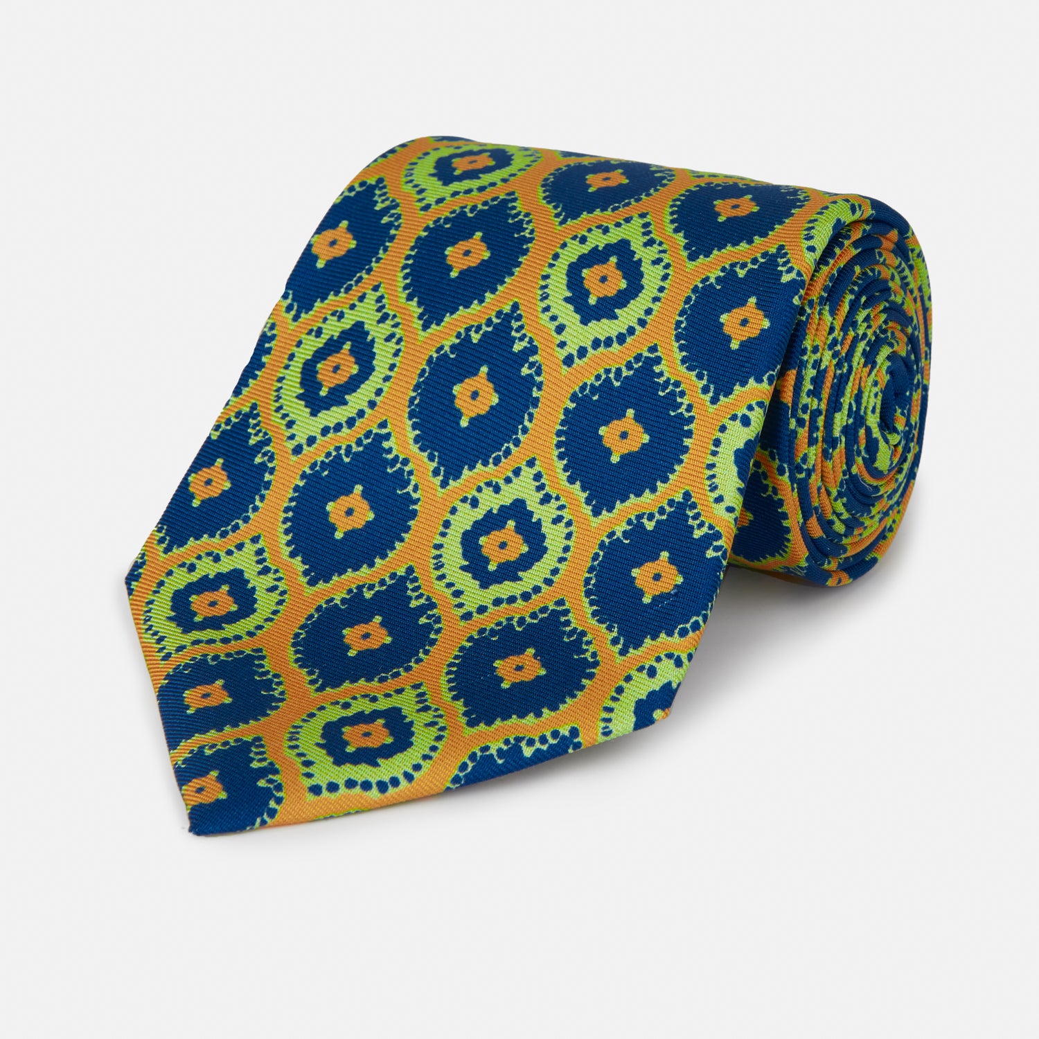 View 1 of product The Yellow Medallion Printed Silk Tie by Turnbull & Asser features a bold abstract medallion pattern in blue, green, and orange on yellow silk, displayed rolled up against a plain white background.