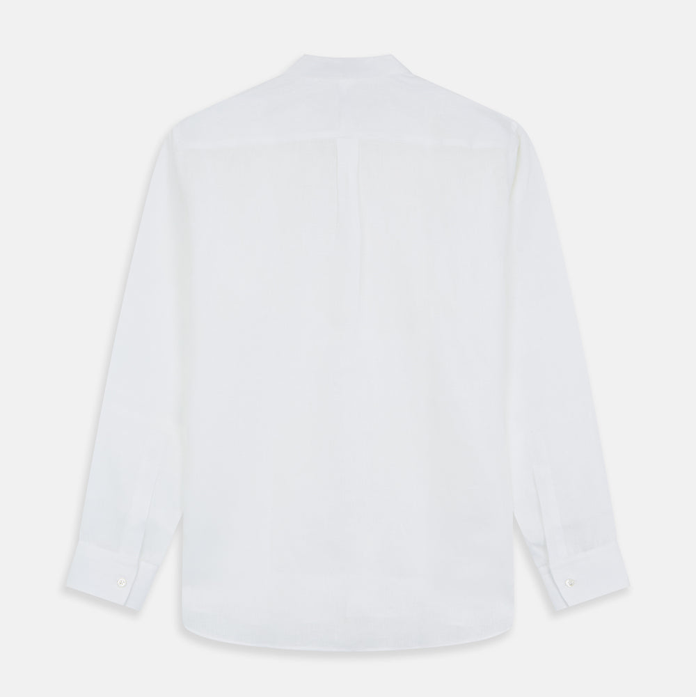 A man stands against a beige background, wearing the Turnbull & Asser White Linen Weekend Fit Blake Shirt, dark trousers, and beige sneakers. With one hand in his pocket and a neutral expression, he captures effortless weekend style.