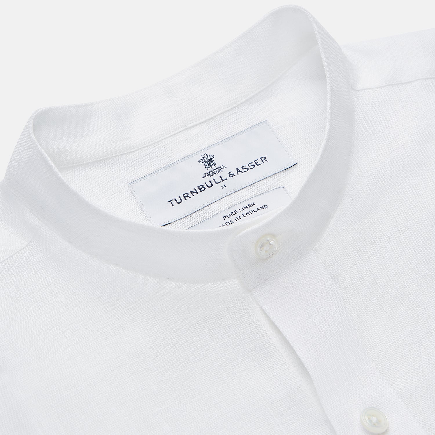 View 3 of product A man stands against a beige background, wearing the Turnbull & Asser White Linen Weekend Fit Blake Shirt, dark trousers, and beige sneakers. With one hand in his pocket and a neutral expression, he captures effortless weekend style.