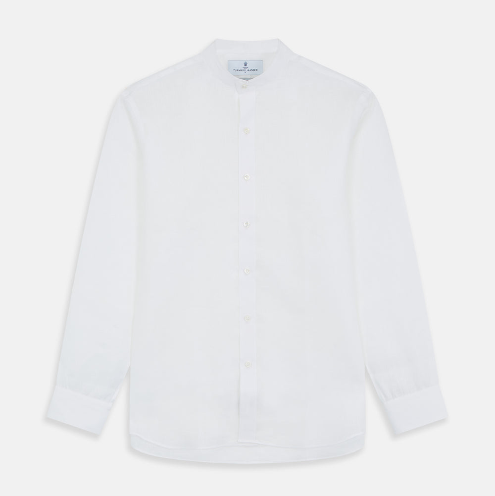 A man stands against a beige background, wearing the Turnbull & Asser White Linen Weekend Fit Blake Shirt, dark trousers, and beige sneakers. With one hand in his pocket and a neutral expression, he captures effortless weekend style.