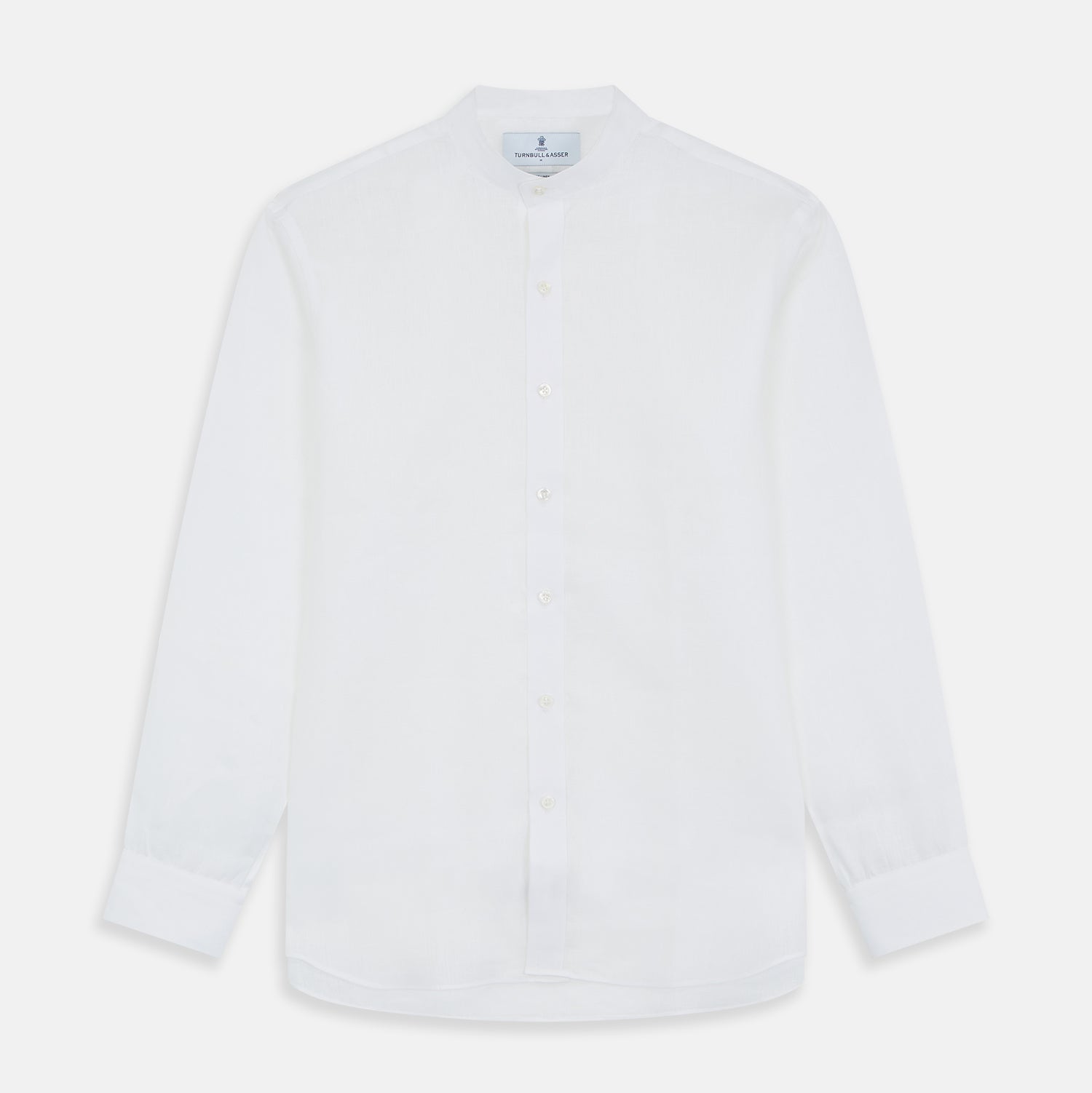 View 2 of product A man stands against a beige background, wearing the Turnbull & Asser White Linen Weekend Fit Blake Shirt, dark trousers, and beige sneakers. With one hand in his pocket and a neutral expression, he captures effortless weekend style.