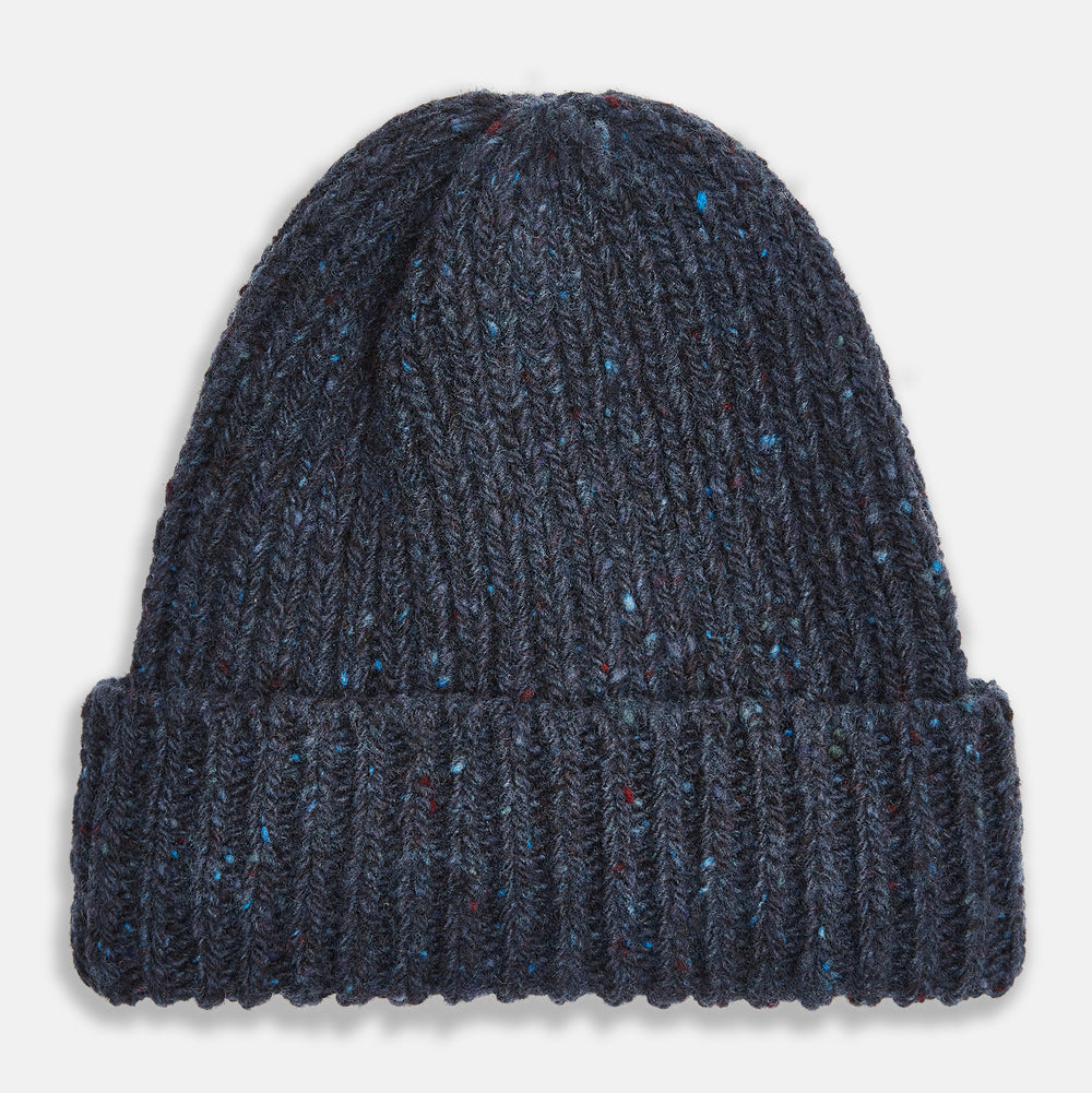 The Turnbull & Asser Navy Donegal Ribbed Merino Hat features thick ribbed knitting, a folded brim, and subtle lighter blue and red flecks throughout the merino yarn, shown against a plain white background.
