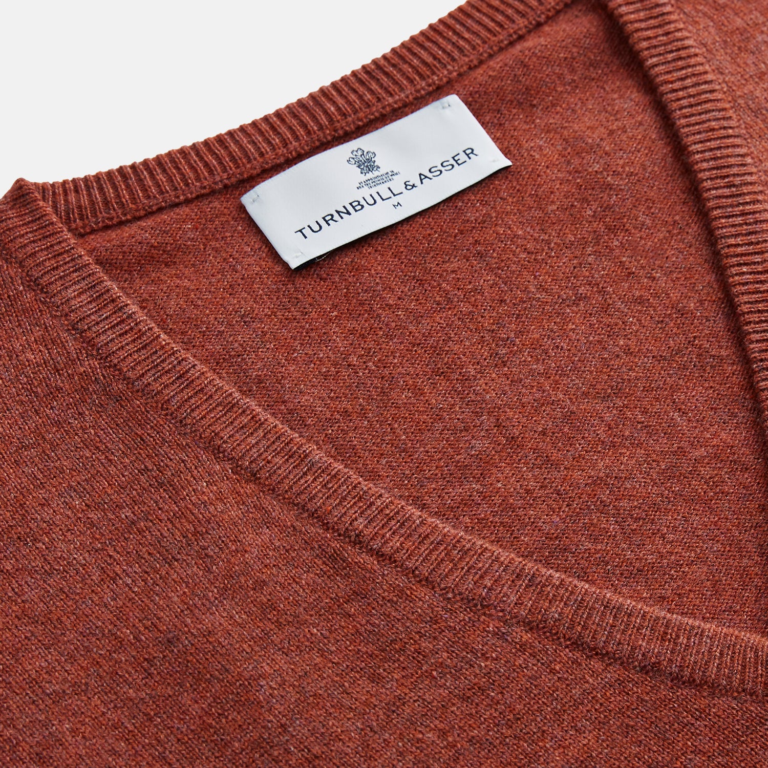 View 2 of product The Turnbull & Asser Burgundy Ifor Cashmere Slipover, a sleeveless V-neck design in fine knit, is shown laid flat on a white background; the neck lining displays a small label, highlighting its Scottish craftsmanship.