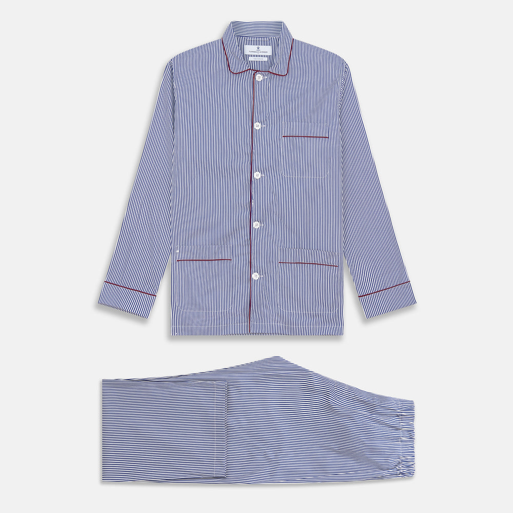 The Turnbull & Asser Navy & White Stripe Cotton Modern Pyjama Set features blue and white Bengal stripes with red piping, a long-sleeve button-up top, chest pocket, and matching pants. Shown laid flat on a white background.