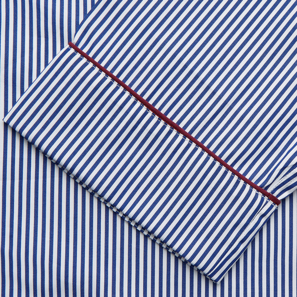 The Turnbull & Asser Navy & White Stripe Cotton Modern Pyjama Set features blue and white Bengal stripes with red piping, a long-sleeve button-up top, chest pocket, and matching pants. Shown laid flat on a white background.