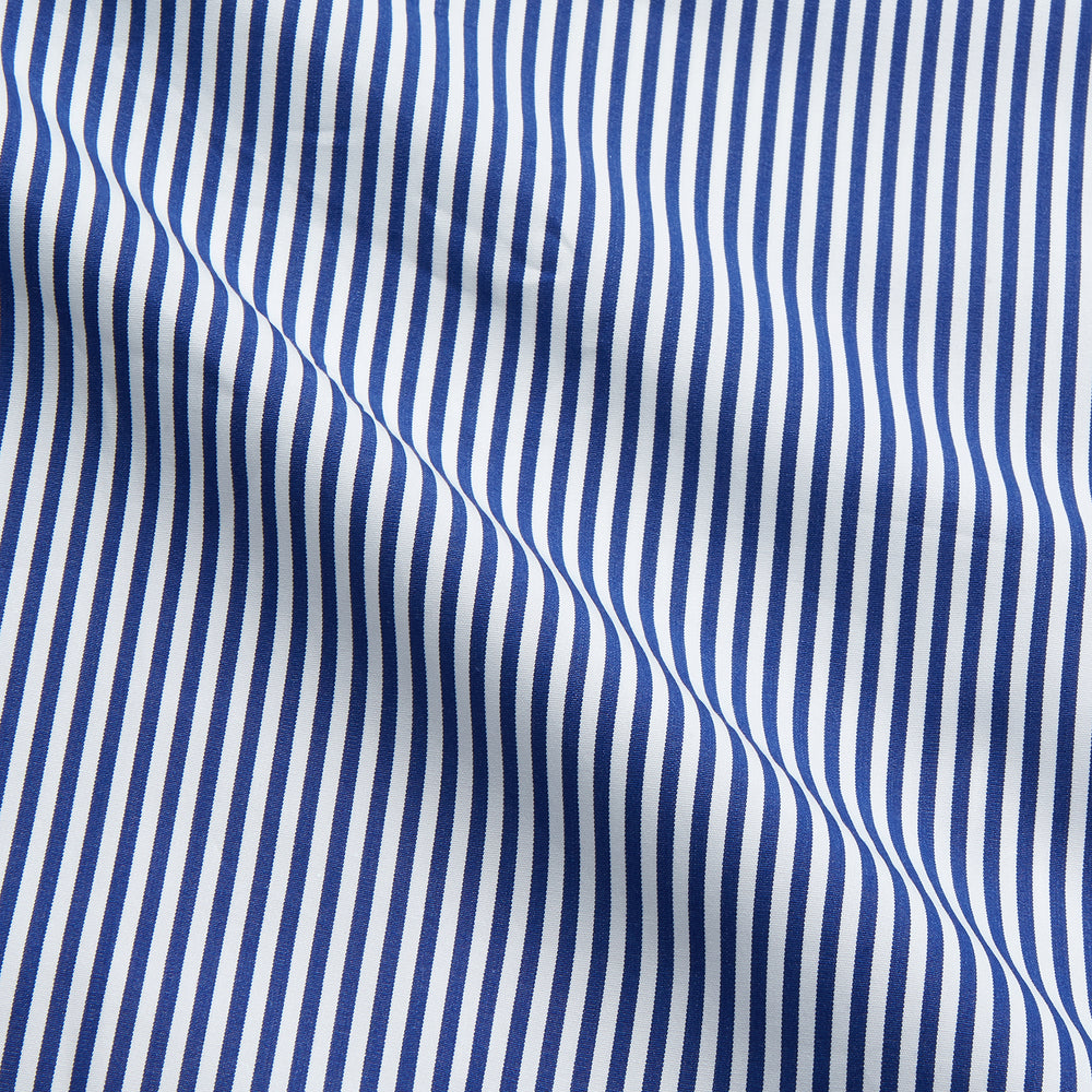 The Turnbull & Asser Navy & White Stripe Cotton Modern Pyjama Set features blue and white Bengal stripes with red piping, a long-sleeve button-up top, chest pocket, and matching pants. Shown laid flat on a white background.