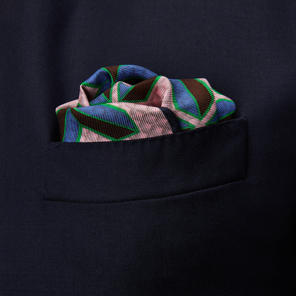 The Pink Multi Crosses Double-Faced Silk Pocket Square by Turnbull & Asser features blue, green, and brown interlocking X-shaped graphics on light pink, with OSINACHI X CJANGO and TURNBULL & ASSER printed at the corners.
