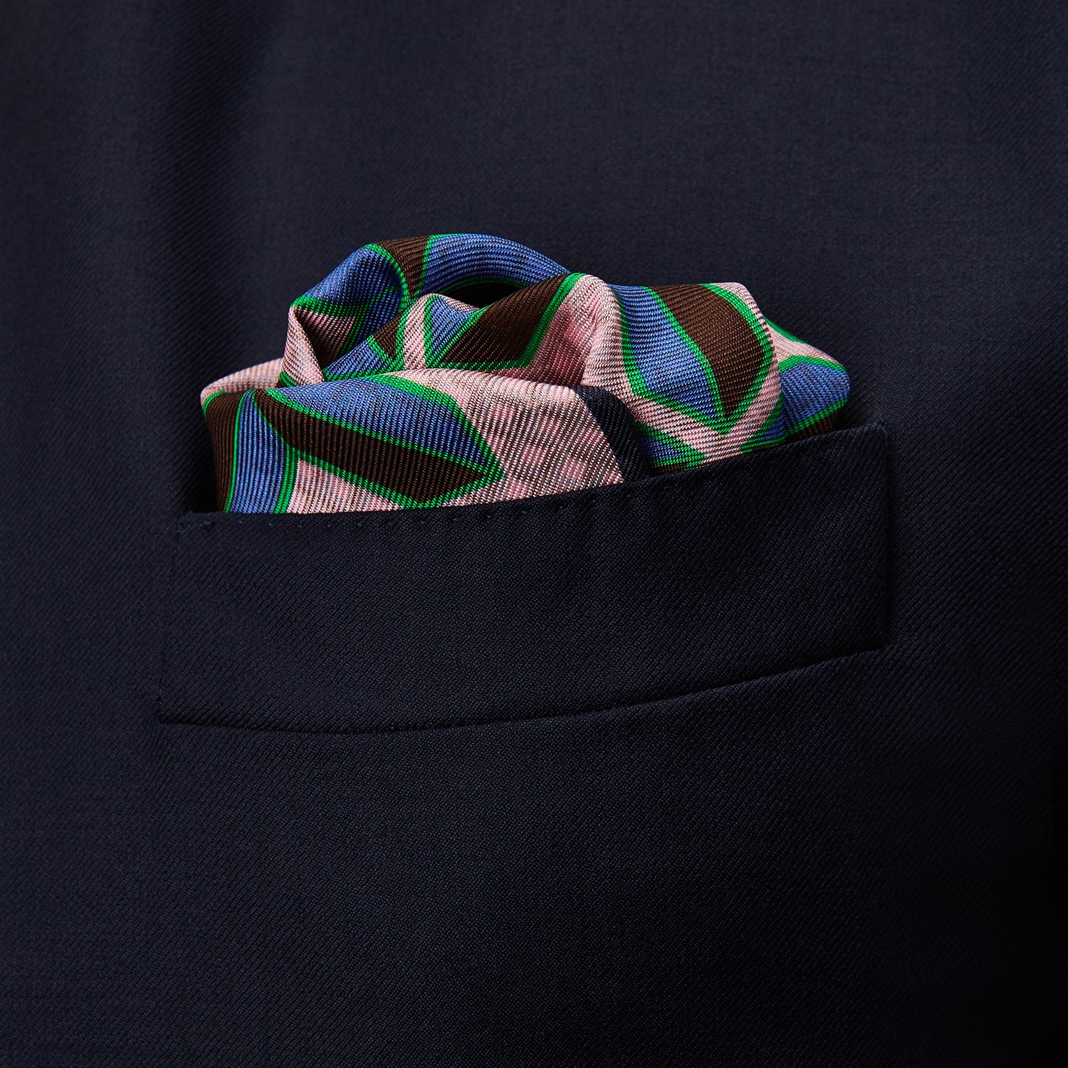 View 3 of product The Pink Multi Crosses Double-Faced Silk Pocket Square by Turnbull & Asser features blue, green, and brown interlocking X-shaped graphics on light pink, with OSINACHI X CJANGO and TURNBULL & ASSER printed at the corners.