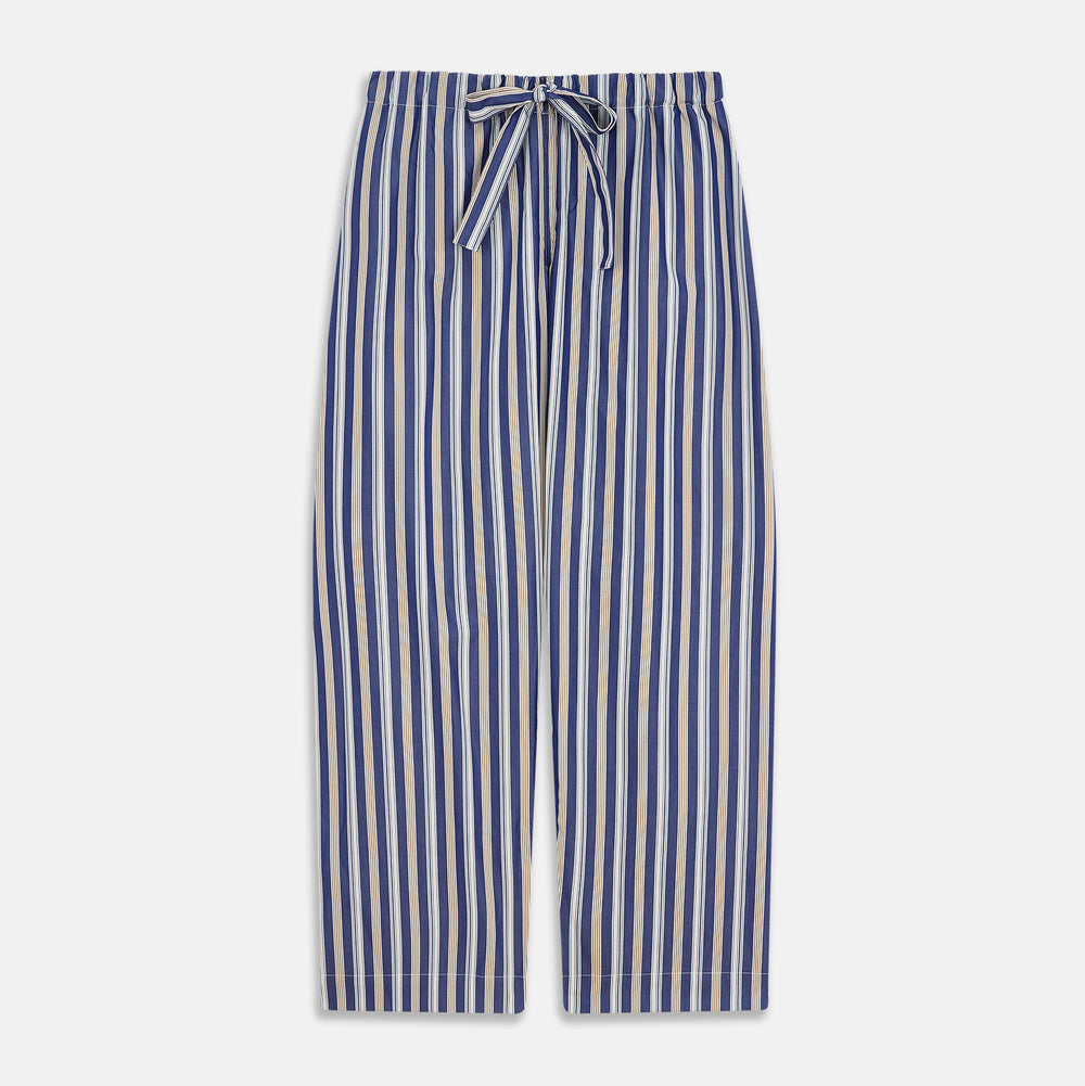 A person stands barefoot on a gray floor in the Turnbull & Asser Blue Multi Stripe Harriet Women’s Pyjama Set with a dark sweater over their shoulders—premium cotton pyjamas that make a perfect gift for her—against a plain beige background.