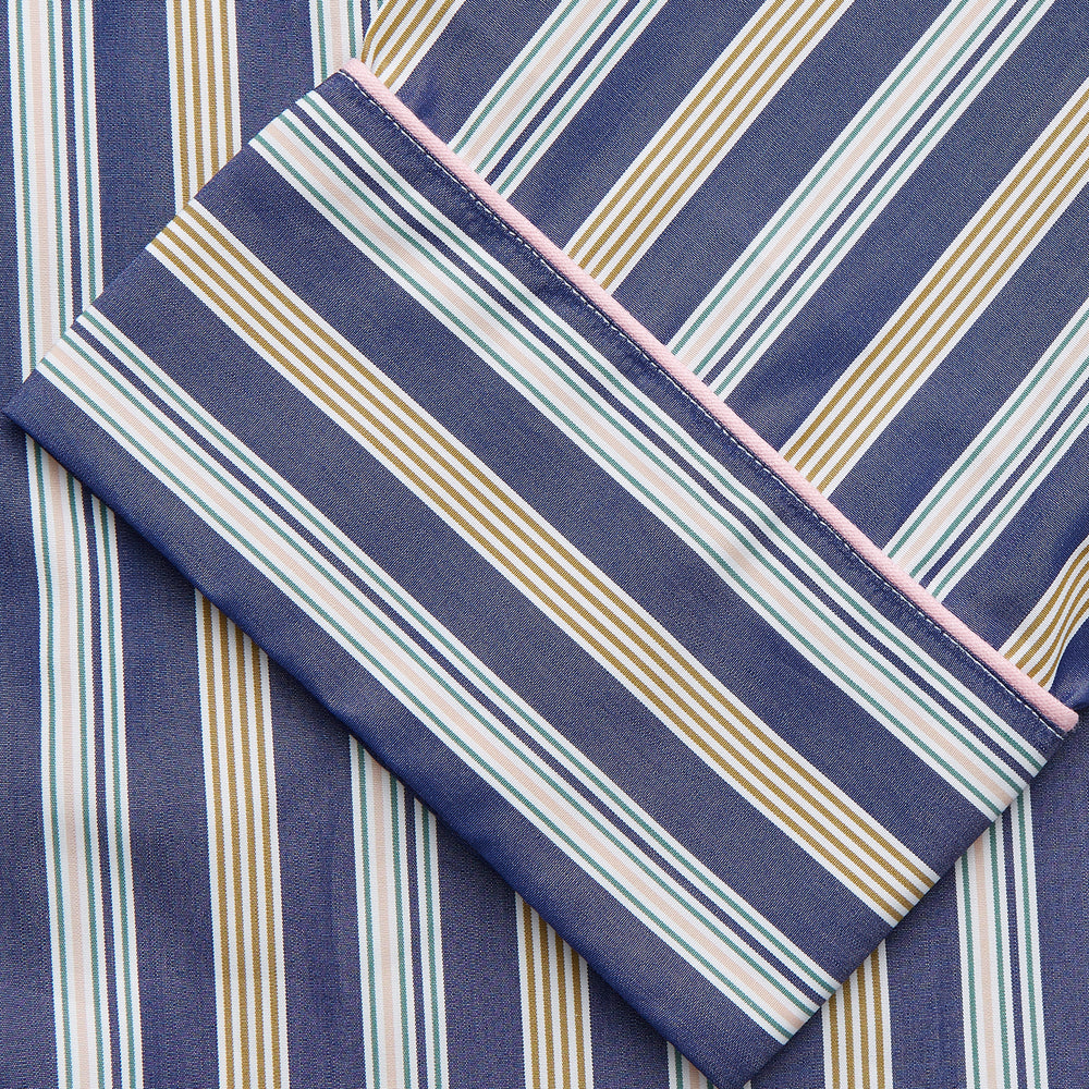 A person stands barefoot on a gray floor in the Turnbull & Asser Blue Multi Stripe Harriet Women’s Pyjama Set with a dark sweater over their shoulders—premium cotton pyjamas that make a perfect gift for her—against a plain beige background.