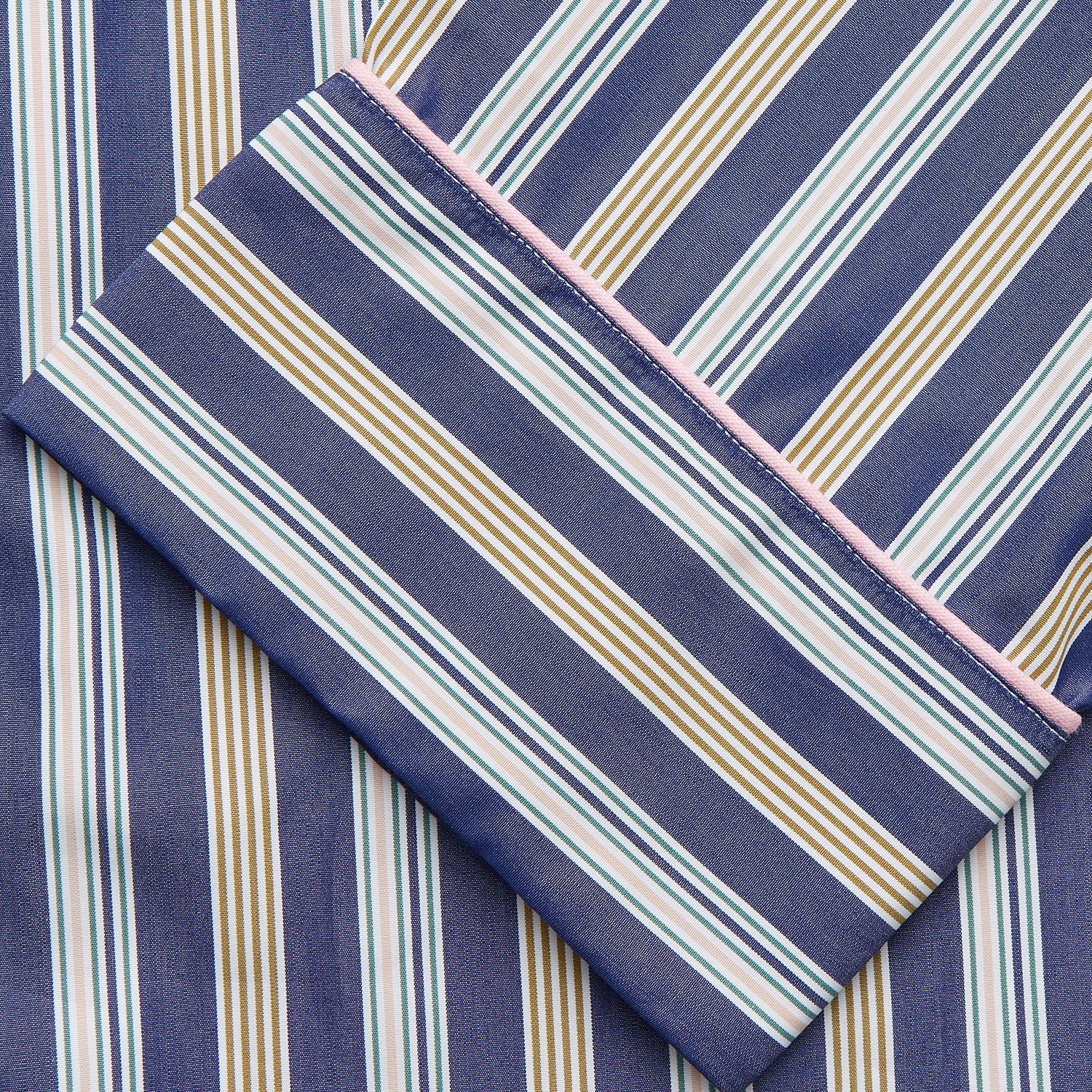 View 6 of product A person stands barefoot on a gray floor in the Turnbull & Asser Blue Multi Stripe Harriet Women’s Pyjama Set with a dark sweater over their shoulders—premium cotton pyjamas that make a perfect gift for her—against a plain beige background.