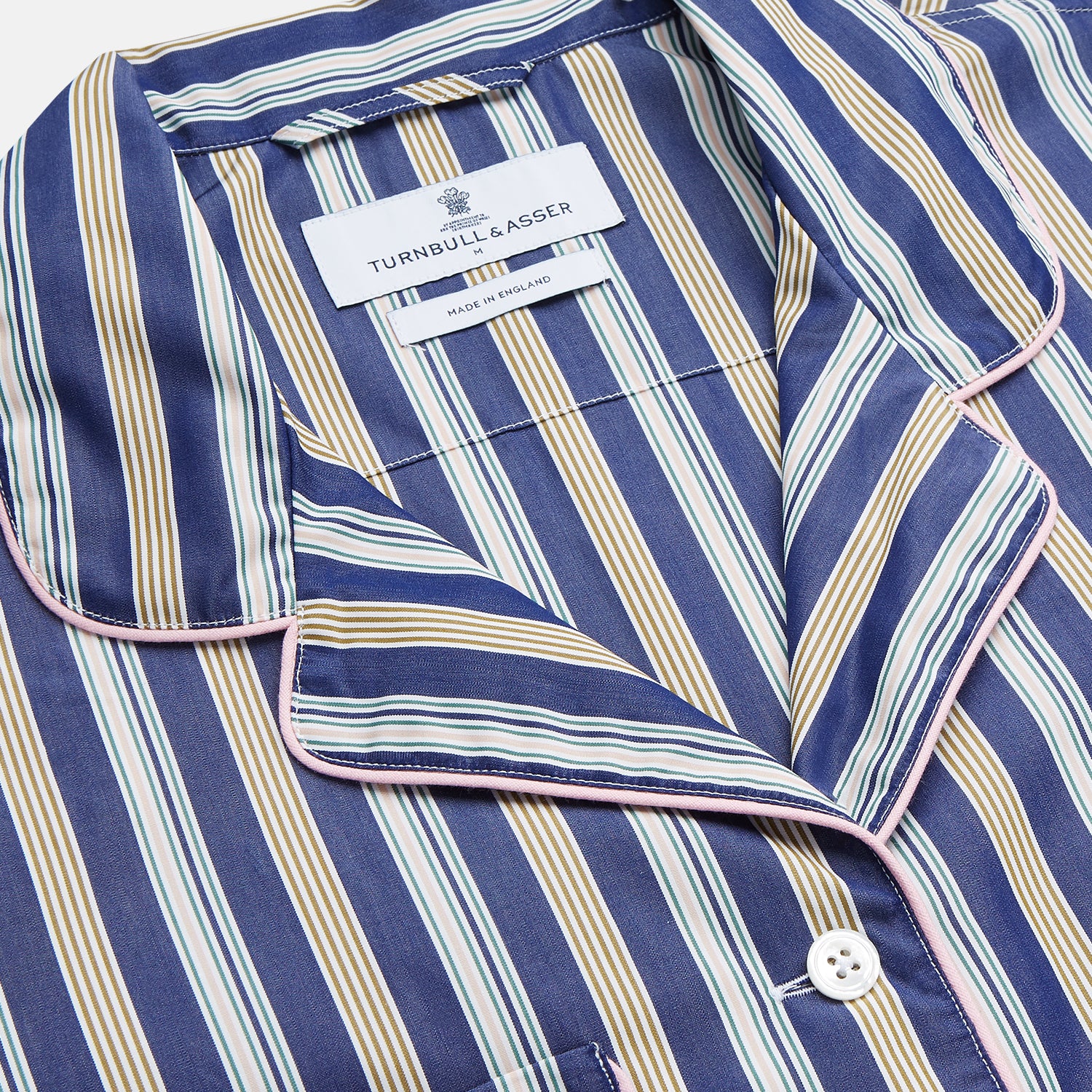 View 5 of product A person stands barefoot on a gray floor in the Turnbull & Asser Blue Multi Stripe Harriet Women’s Pyjama Set with a dark sweater over their shoulders—premium cotton pyjamas that make a perfect gift for her—against a plain beige background.