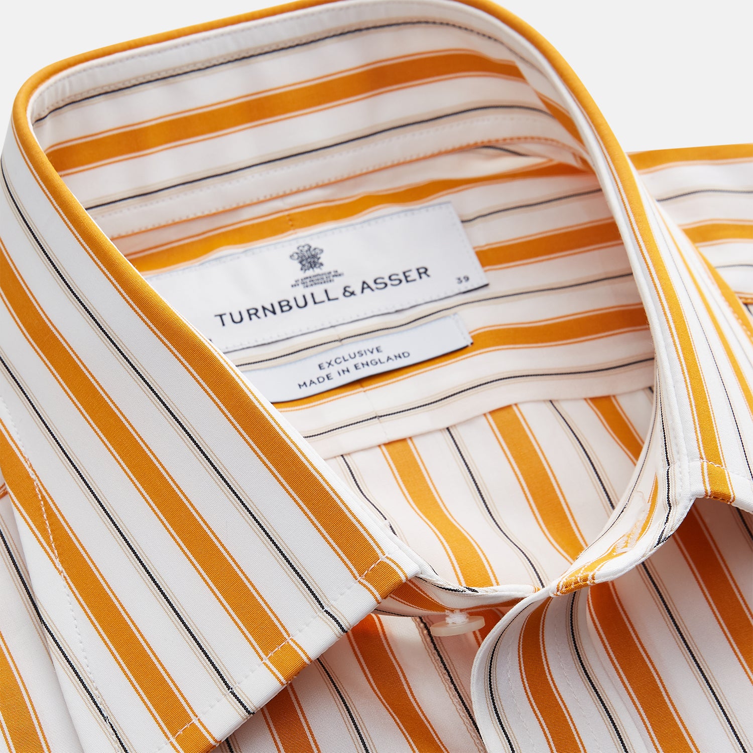 View 4 of product A man stands against a tan background wearing a Turnbull & Asser Orange Multi Stripe Regular Fit Shirt with T&A Collar and 3 Button Cuffs, paired with tan dress pants, brown belt, and brown shoes. He faces forward with a neutral expression.