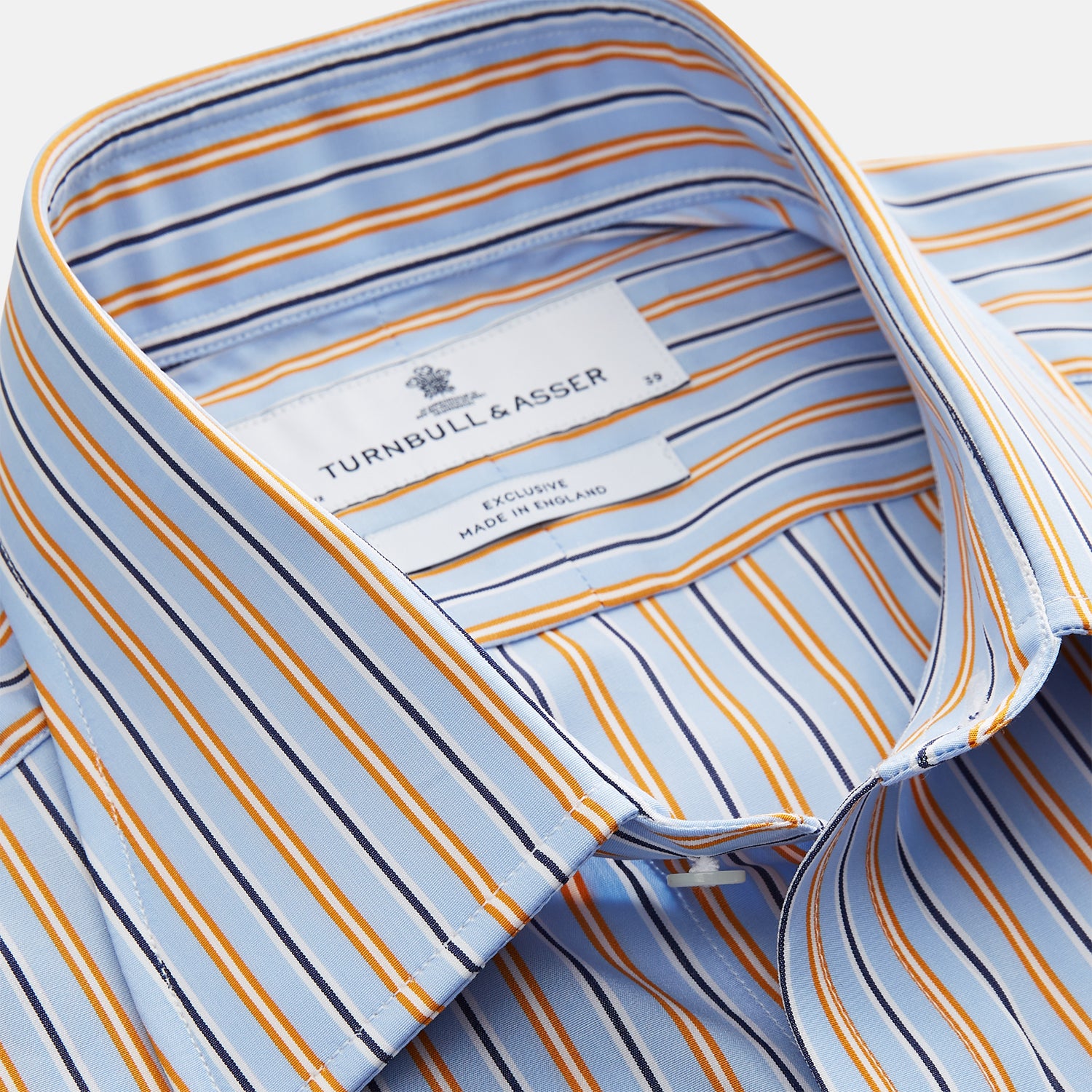 View 3 of product A man stands against a beige background, wearing a Turnbull & Asser Blue, Orange & Navy Multi Stripe Regular Fit Shirt with T&A collar and 3-button cuffs, tucked into tan dress pants with a black belt. He faces forward with a neutral expression.