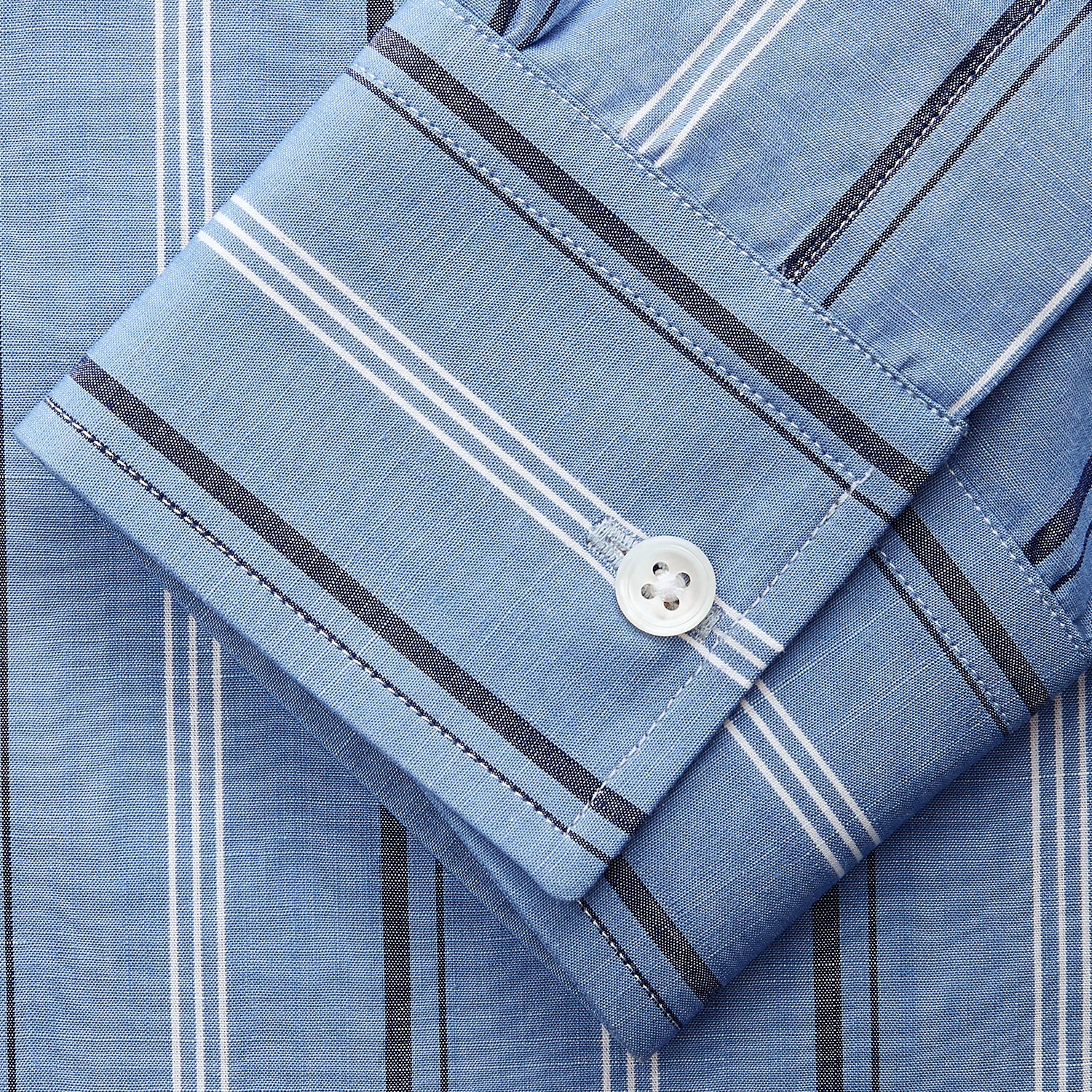 View 4 of product A man stands against a plain tan background wearing Turnbull & Asser's Blue Multi Chambray Stripe Weekend Fit Shirt with a Derby collar and 1 button cuffs, paired with a red patterned tie and gray trousers. His hands are in his pockets.