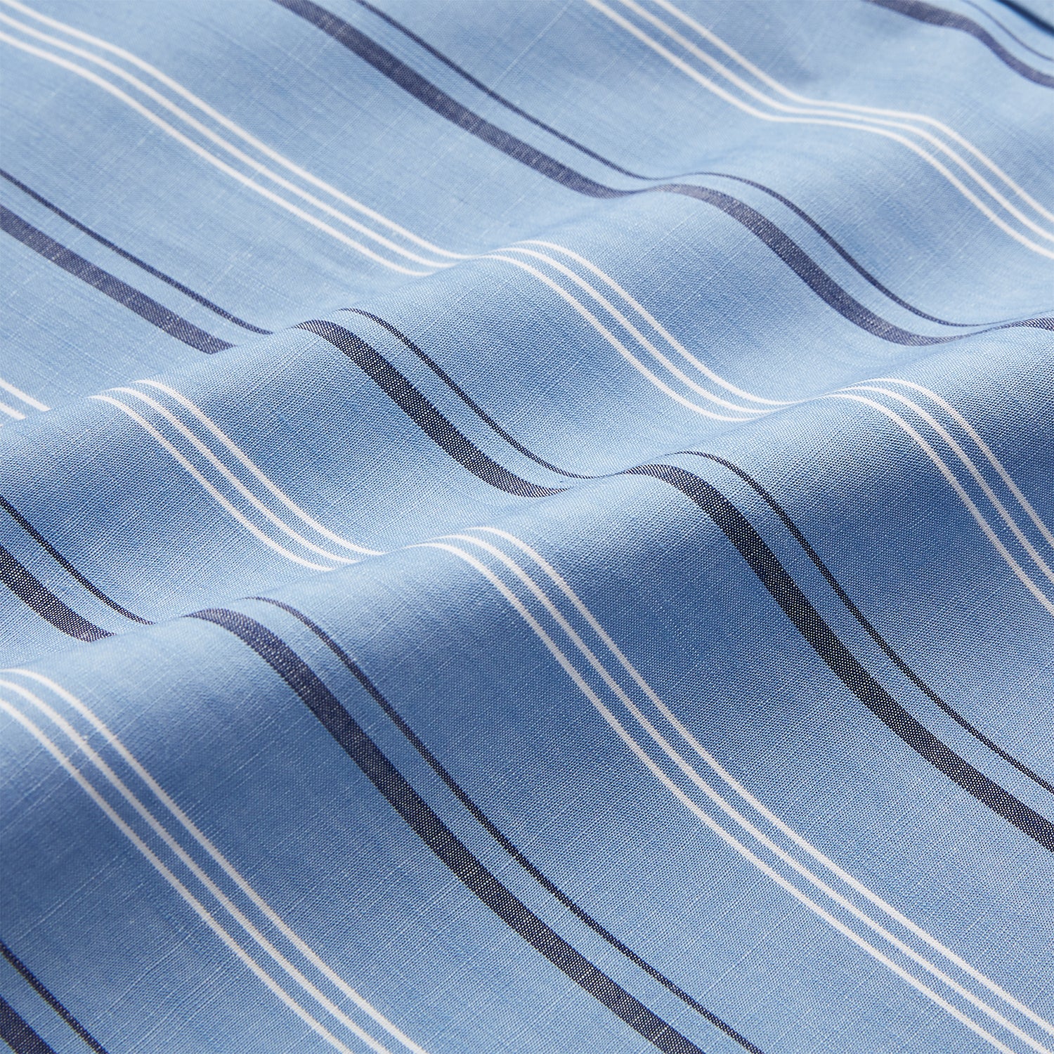 View 5 of product A man stands against a plain tan background wearing Turnbull & Asser's Blue Multi Chambray Stripe Weekend Fit Shirt with a Derby collar and 1 button cuffs, paired with a red patterned tie and gray trousers. His hands are in his pockets.