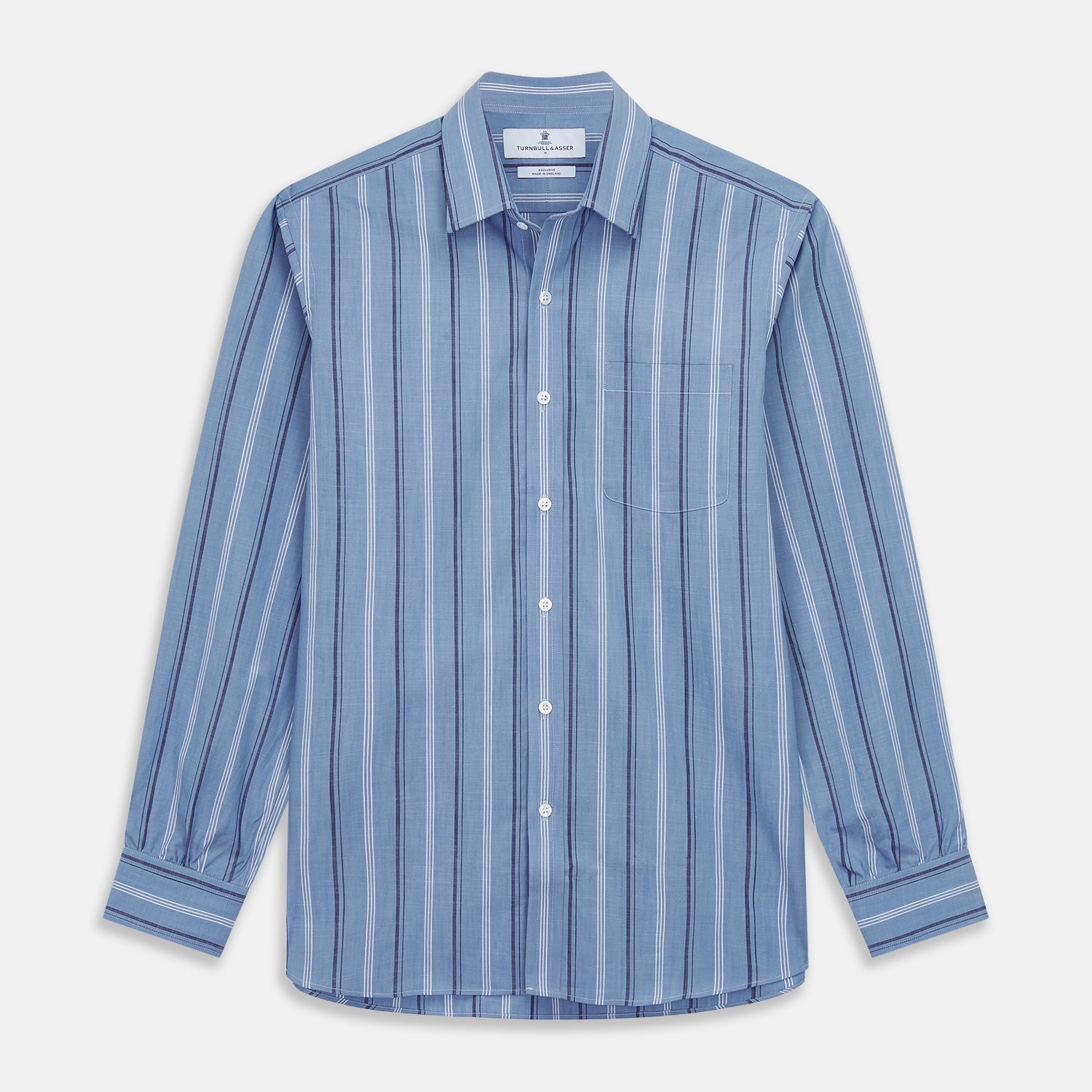 View 2 of product A man stands against a plain tan background wearing Turnbull & Asser's Blue Multi Chambray Stripe Weekend Fit Shirt with a Derby collar and 1 button cuffs, paired with a red patterned tie and gray trousers. His hands are in his pockets.