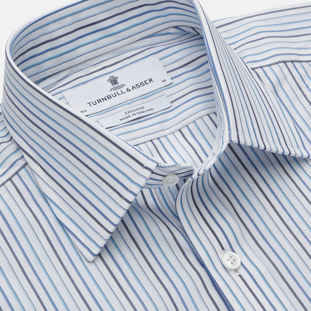 The Turnbull & Asser Blue Multi Blazer Stripe Regular Fit Mayfair Shirt features light blue and white vertical stripes, a signature Mayfair collar, and is neatly displayed on a white background.