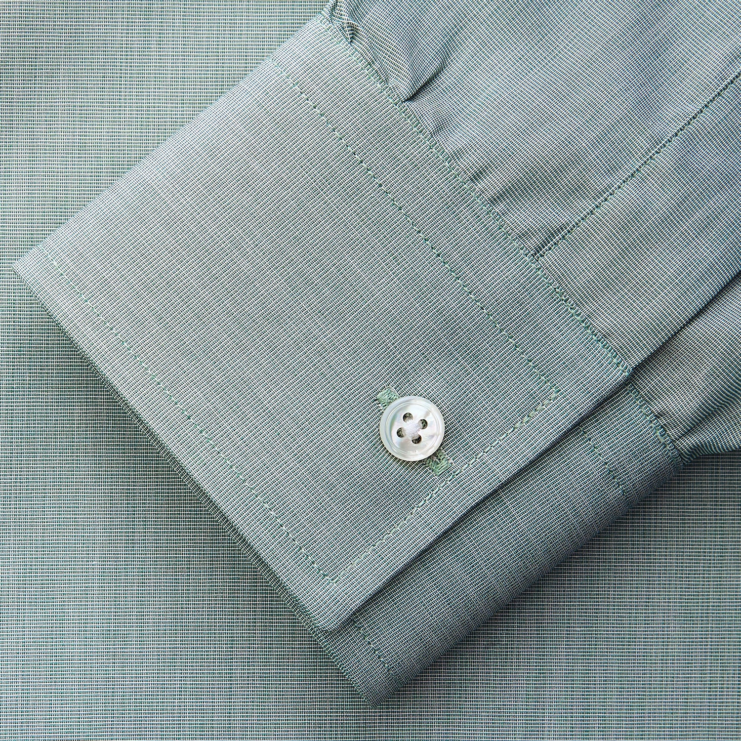 View 5 of product A man stands against a beige background wearing a Turnbull & Asser Green Weekend Fit Shirt with Long Point Collar and Single Button Cuffs, paired with a striped tie, dark trousers, and black dress shoes, hands in pockets and a neutral expression.