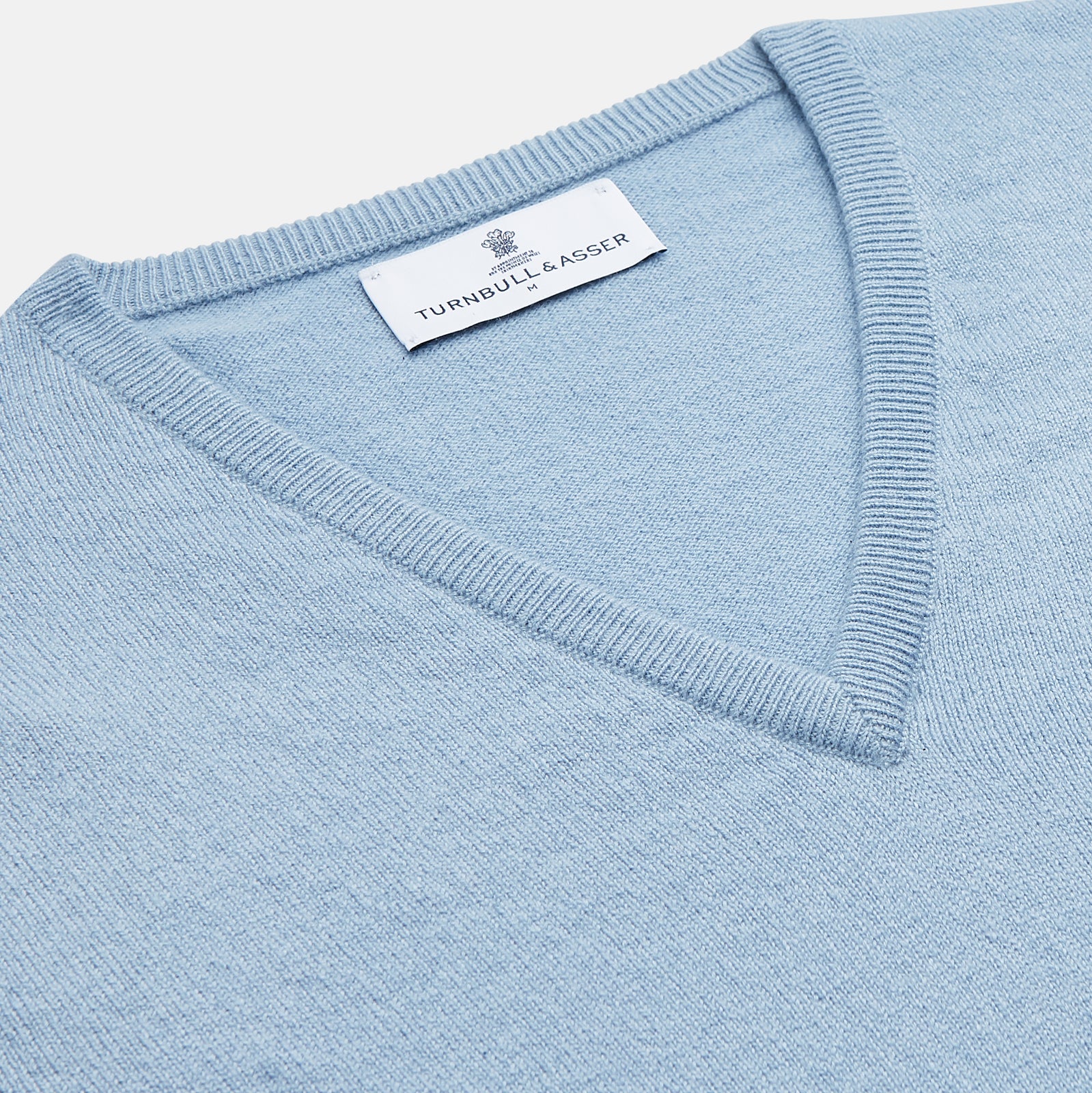 View 2 of product The Turnbull & Asser Pale Blue Cashmere Ifor Slipover is a sleeveless V-neck sweater vest with ribbed edges, shown laid flat on a white background—a classic menswear staple.