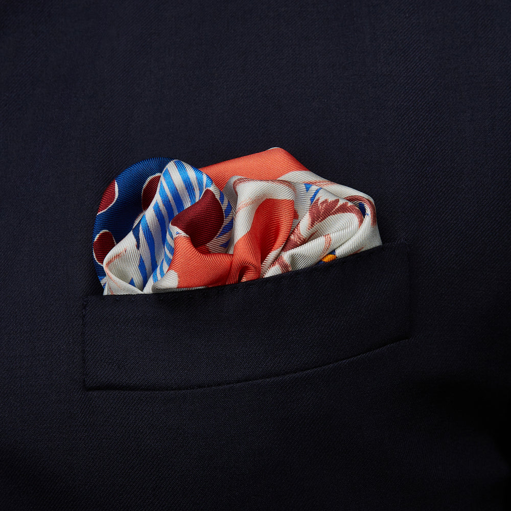 The Pink and Red Lily Silk Pocket Square by Turnbull & Asser features a vibrant, hand-drawn floral design with large lilies and abstract shapes in pink, white, blue, and yellow on pale blue vertical stripes.
