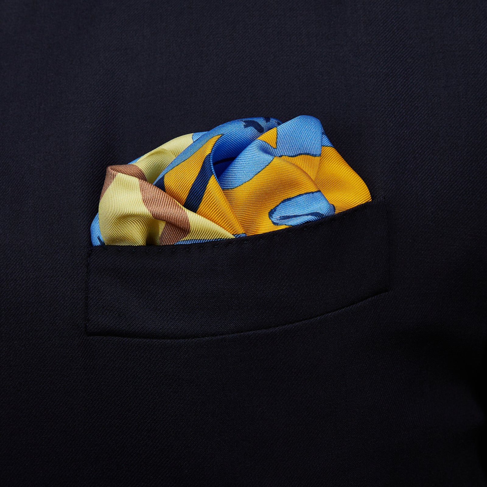 View 2 of product The Blue and Yellow Lily Silk Pocket Square by Turnbull & Asser features a vibrant, hand-drawn design of large blue lilies with dark stems on a yellow background adorned with pale blue stripes and tan abstract shapes.