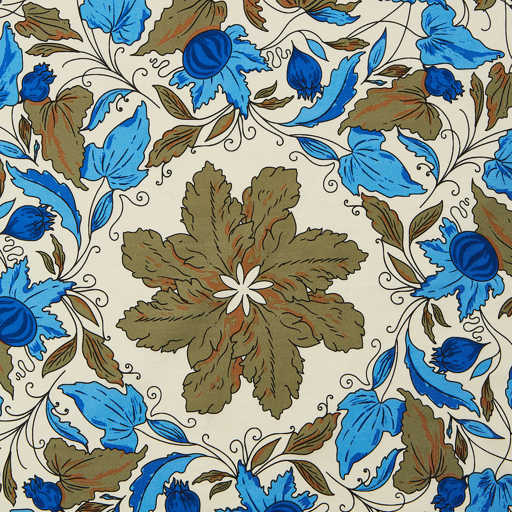 The Turnbull & Asser Pale Blue and Oat Foliage Pattern Silk Pocket Square is crafted in England, featuring a cream background with a circular blue and green floral design, bordered edges, and the brand's logo in one corner.