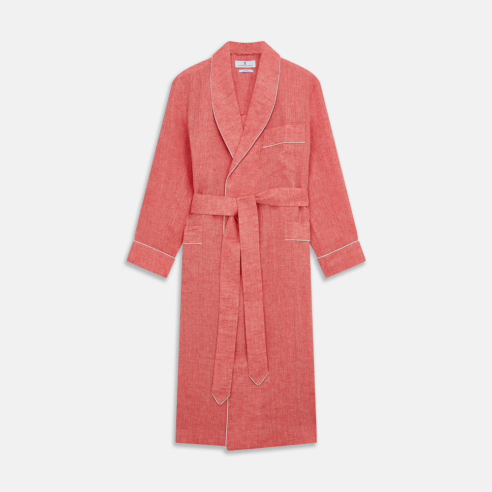 The Pink Linen Arnold Gown by Turnbull & Asser features white piping, long sleeves, a shawl collar, chest pocket, and a wrap-around belt tied at the waist, shown on a white background.