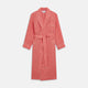 The Pink Linen Arnold Gown by Turnbull & Asser features white piping, long sleeves, a shawl collar, chest pocket, and a wrap-around belt tied at the waist, shown on a white background.