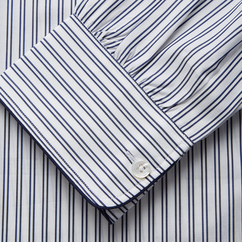 The Turnbull & Asser White and Navy Striped Cotton Sussex Nightshirt features long sleeves, a knee-length cut, a collar, front buttons, a chest pocket with dark trim, and a curved hem for modern comfort inspired by tradition.