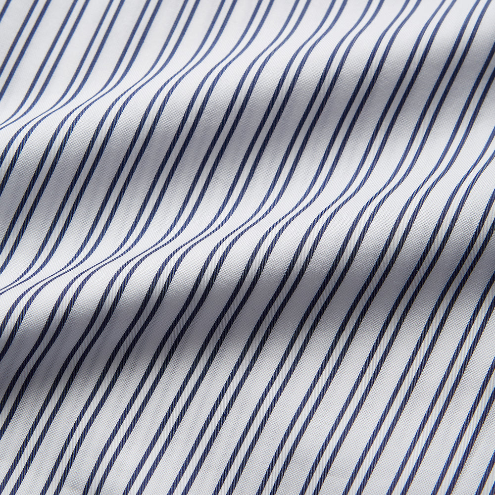 The Turnbull & Asser White and Navy Striped Cotton Sussex Nightshirt features long sleeves, a knee-length cut, a collar, front buttons, a chest pocket with dark trim, and a curved hem for modern comfort inspired by tradition.