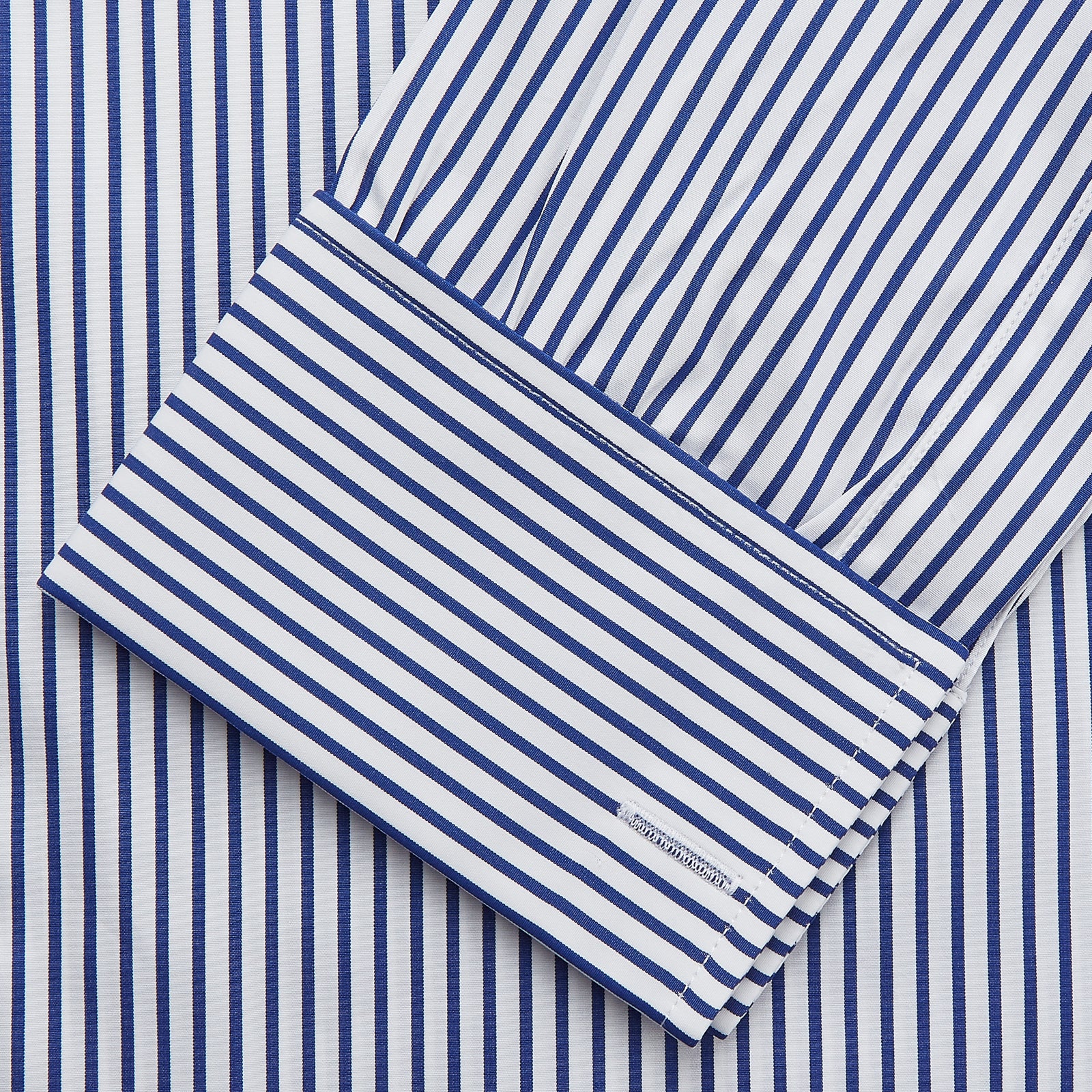 View 3 of product The Turnbull & Asser Navy Stripe Cotton Regular Fit Whitby Shirt features vertical blue and white stripes, long sleeves, a collar, double cuffs, and a button-down front, shown laid flat on a white background.
