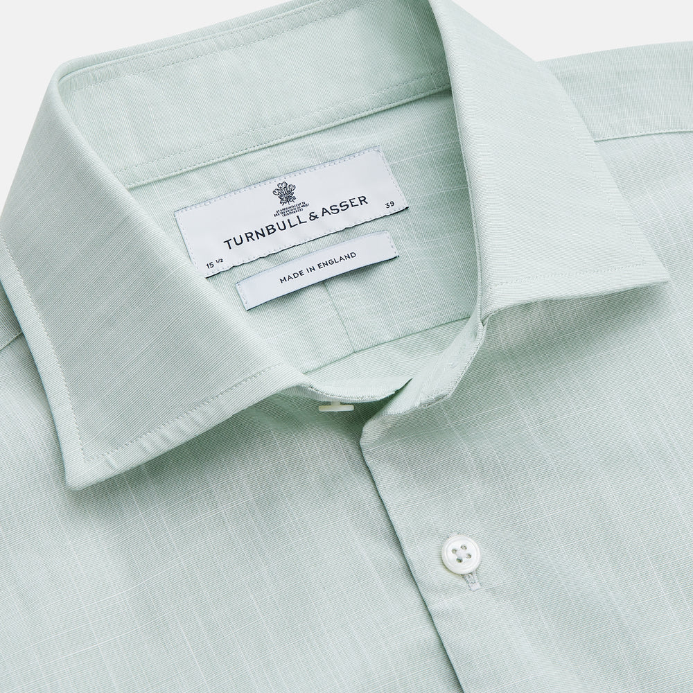 The Turnbull & Asser Light Green Chambray Tailored Fit Shelton Shirt features long sleeves, a classic collar, and white buttons—an elegant men's formal shirt shown neatly laid flat on a white background.