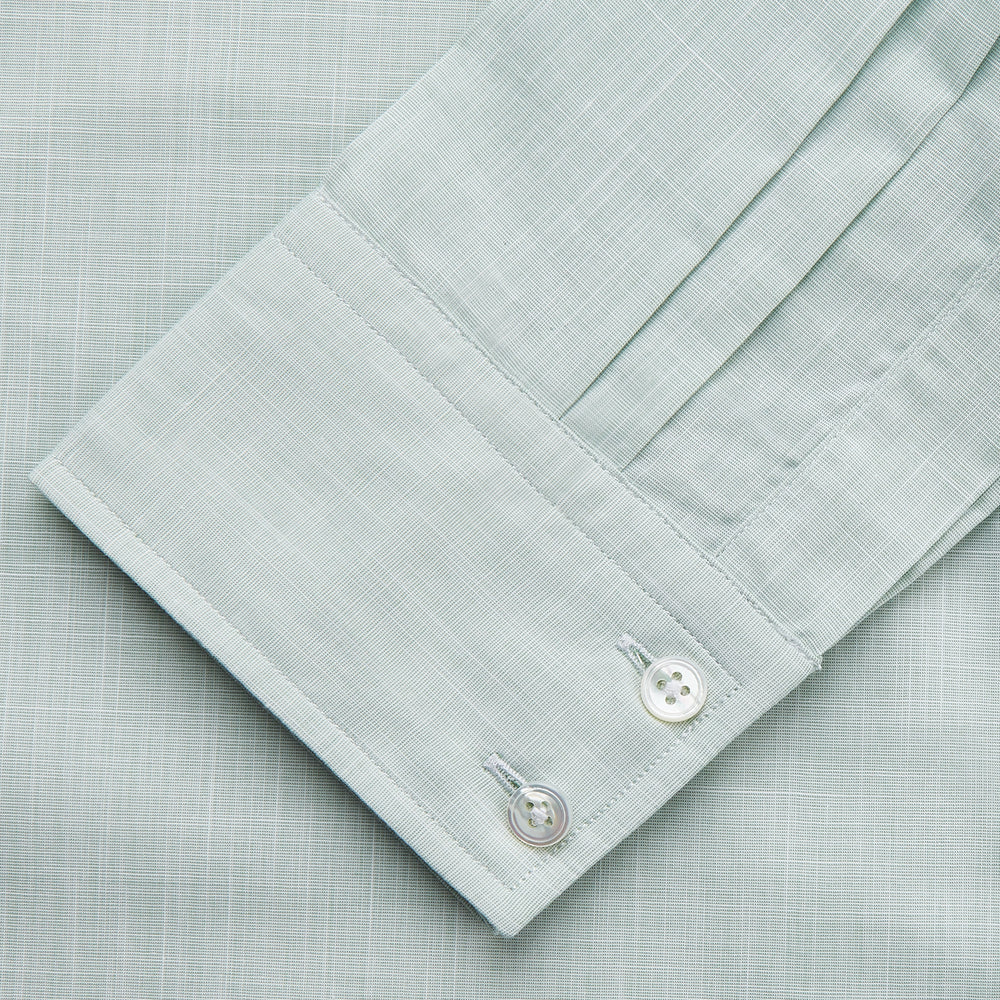 The Turnbull & Asser Light Green Chambray Tailored Fit Shelton Shirt features long sleeves, a classic collar, and white buttons—an elegant men's formal shirt shown neatly laid flat on a white background.