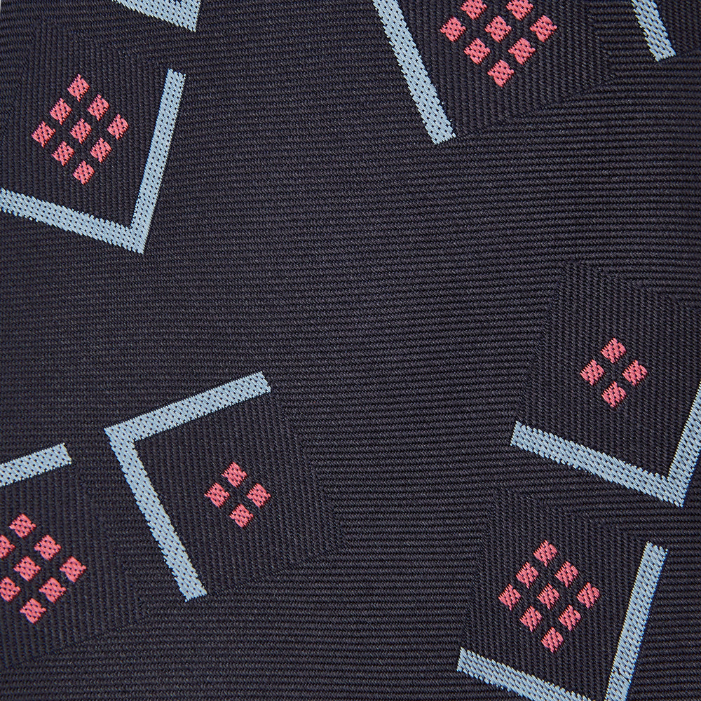 A Turnbull & Asser Navy Graphic Deco Silk Tie, featuring light blue chevrons and red squares on a dark navy background, shown rolled up against a plain white backdrop.