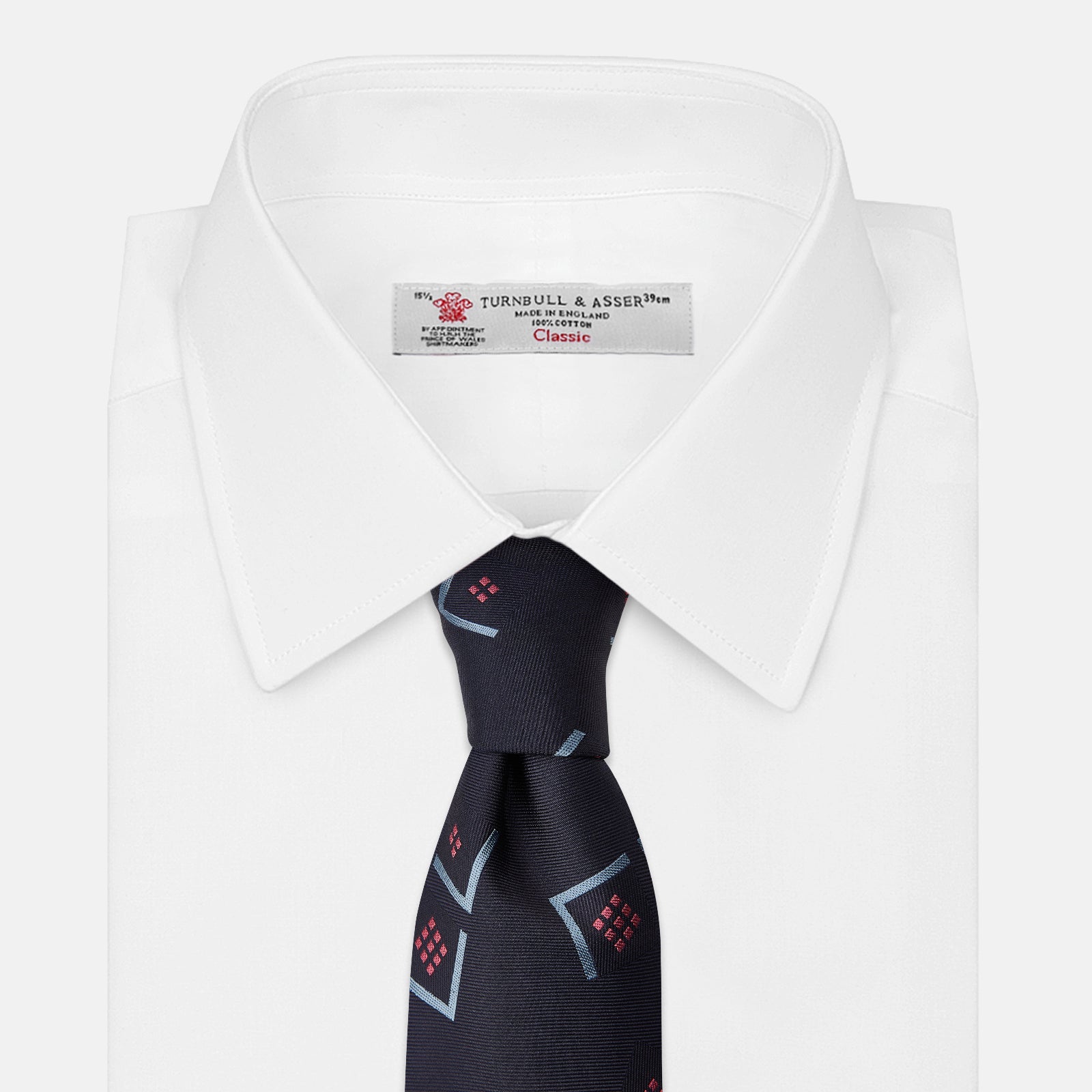 View 4 of product A Turnbull & Asser Navy Graphic Deco Silk Tie, featuring light blue chevrons and red squares on a dark navy background, shown rolled up against a plain white backdrop.