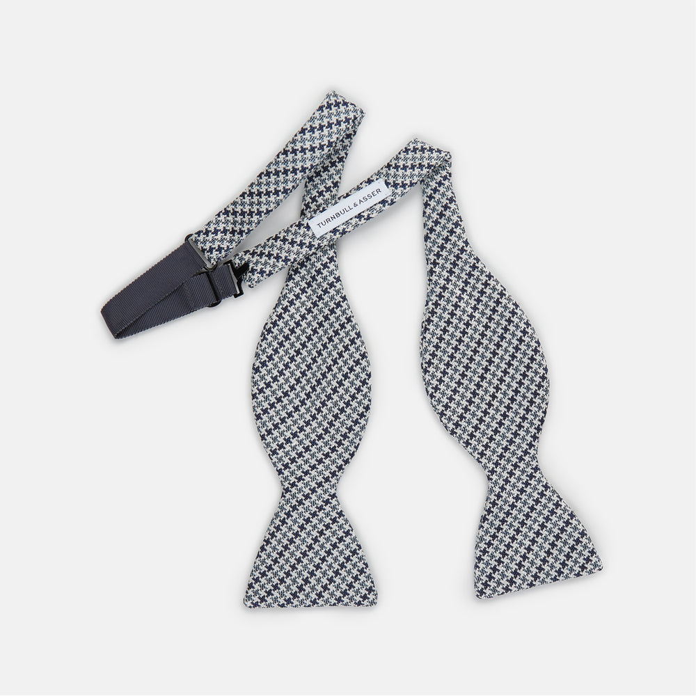 The Turnbull & Asser Blue Multi Puppytooth Silk Bow Tie features a classic puppytooth pattern in shades of blue, displayed against a plain white background.
