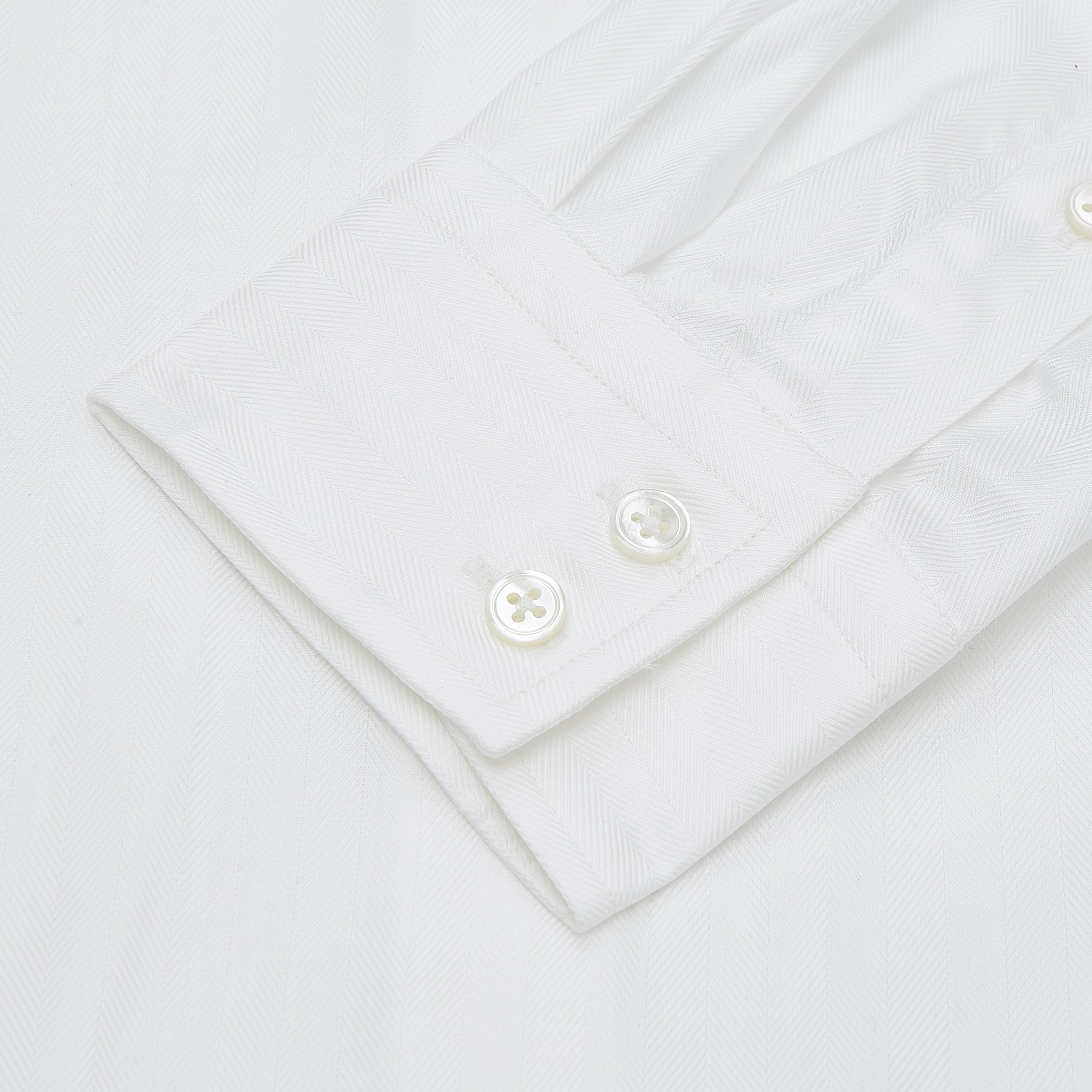 View 2 of product The Turnbull & Asser White Herringbone Tailored Fit Cotton Shirt features a long point collar, 2-button cuff, and button-down front, shown laid flat on a white background.