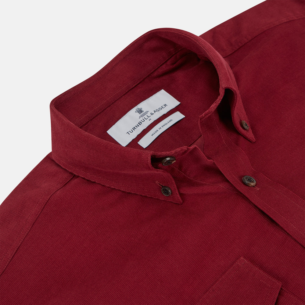 The Turnbull & Asser Burgundy Corduroy Officer Weekend Fit Shirt features a Dorset collar, long sleeves, one-button cuffs, and two chest pockets with buttoned flaps, shown laid flat on a white background.