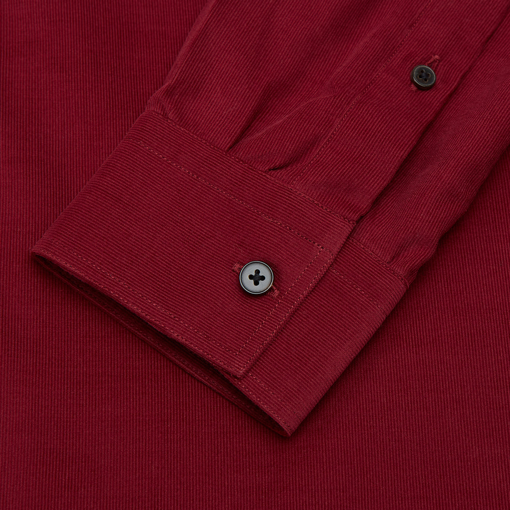 The Turnbull & Asser Burgundy Corduroy Officer Weekend Fit Shirt features a Dorset collar, long sleeves, one-button cuffs, and two chest pockets with buttoned flaps, shown laid flat on a white background.