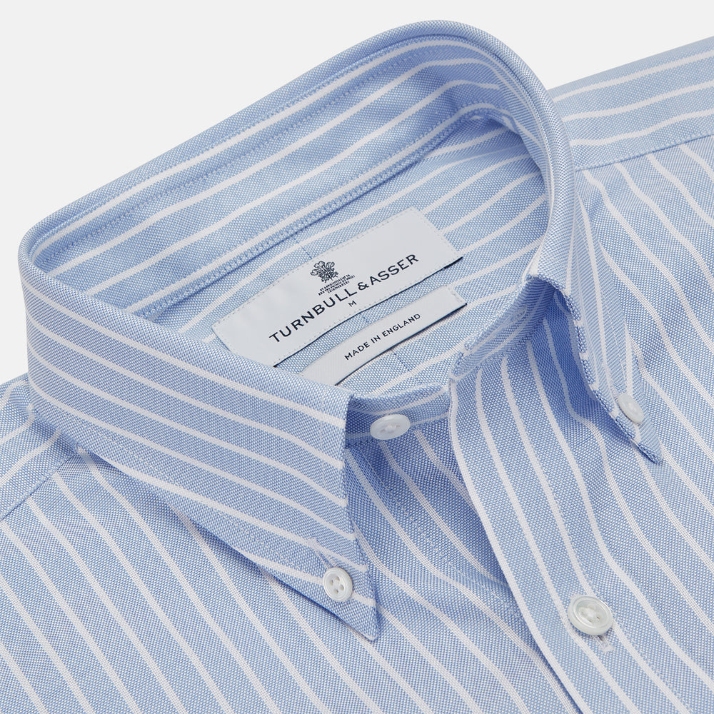The Turnbull & Asser Blue and White Broad Stripe Oxford Weekend Fit Shirt features a Dorset collar, 1-button cuffs, and classic stripes—ideal for smart-casual days. Laid flat on a white background.