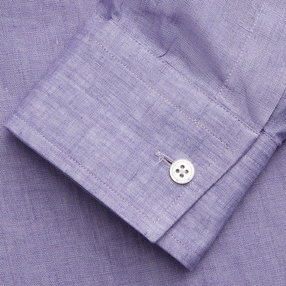 A man stands against a beige background wearing the Turnbull & Asser Lilac Weekend Fit Linen Blake Shirt with Stand Collar and 1-Button Cuffs, paired with dark pinstriped pants and brown sandals—a relaxed weekend look.