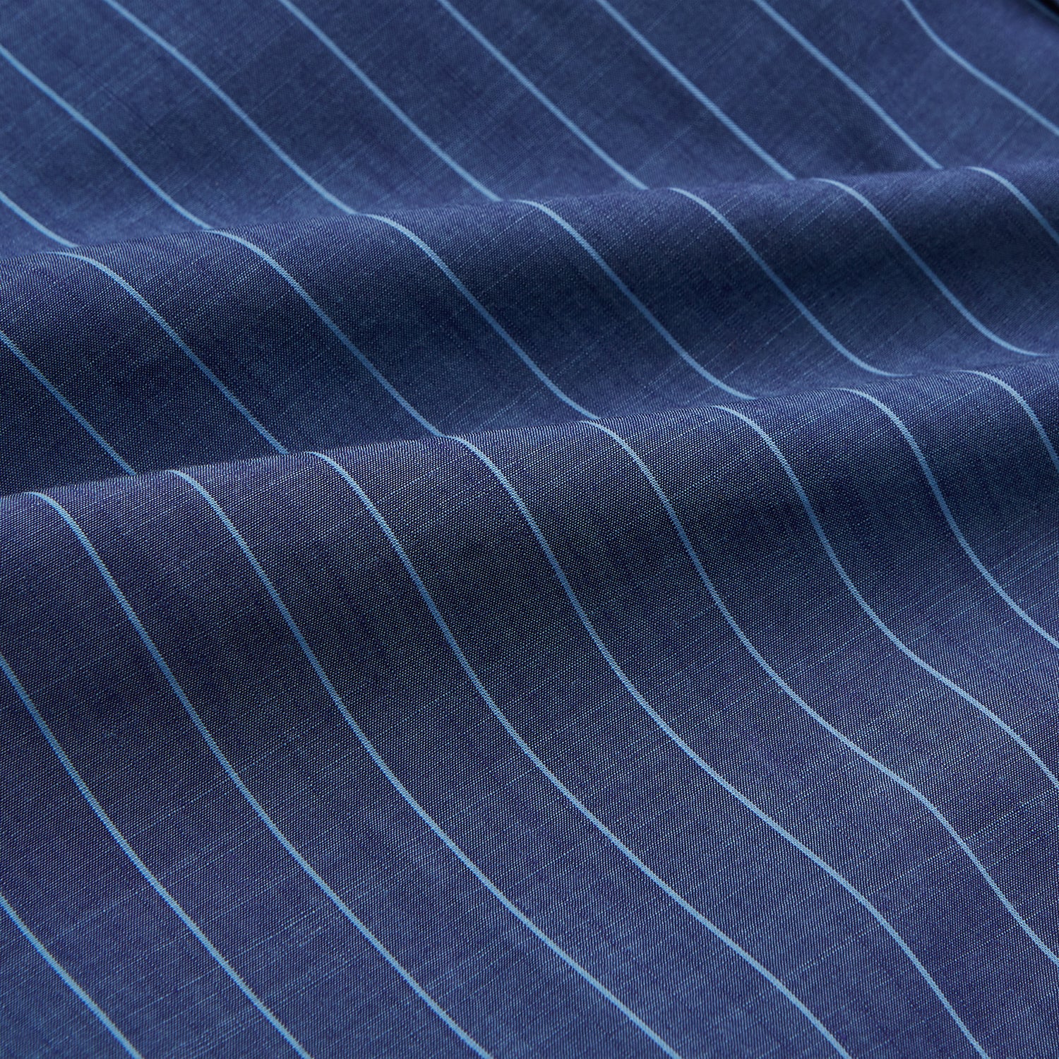 View 5 of product Close-up of a person wearing the Turnbull & Asser Blue Stripe Weekend Fit Nevis Shirt with Derby Collar and 1-Button Cuffs under a dark pinstripe blazer, focusing on the collar and upper chest. The face is partially out of frame.