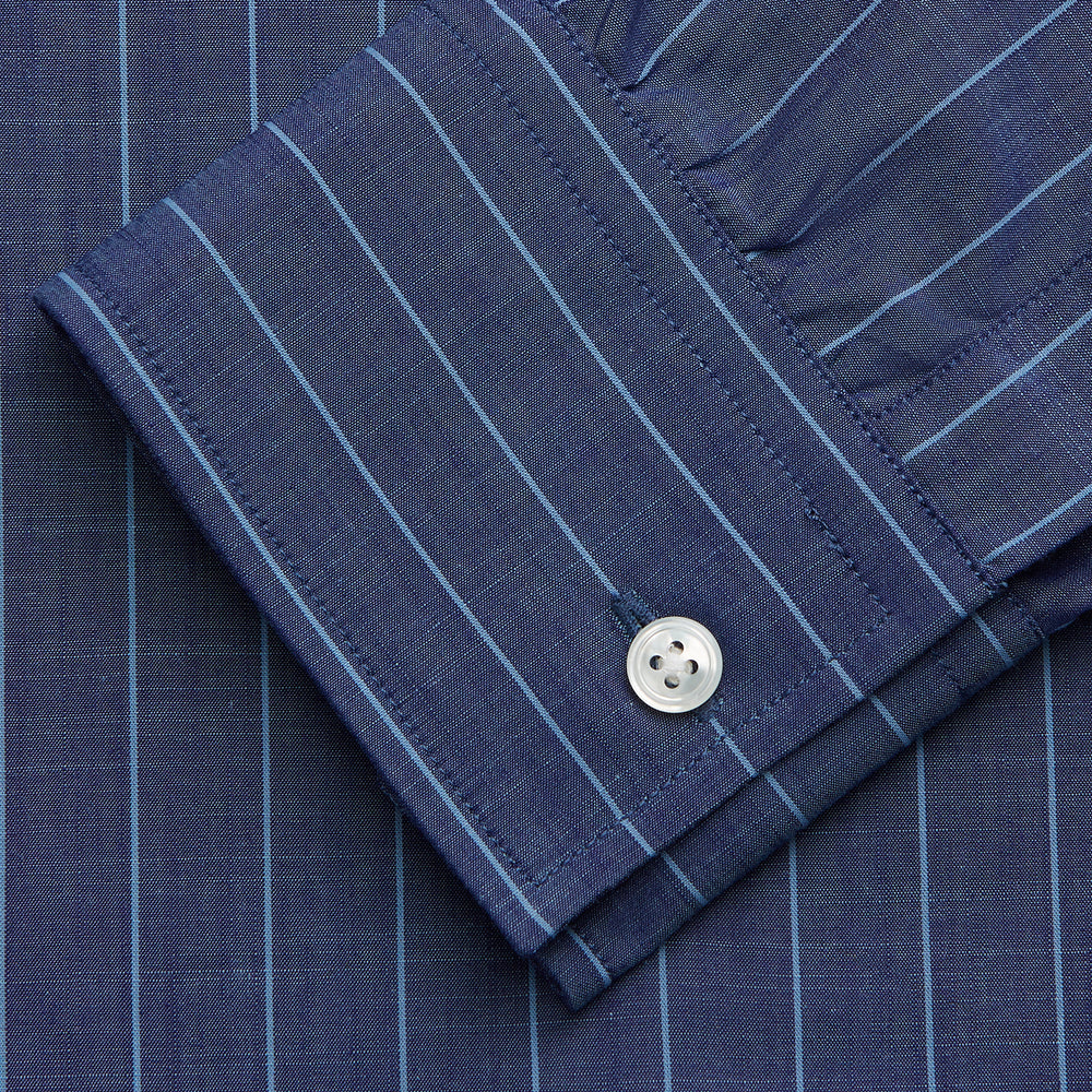 Close-up of a person wearing the Turnbull & Asser Blue Stripe Weekend Fit Nevis Shirt with Derby Collar and 1-Button Cuffs under a dark pinstripe blazer, focusing on the collar and upper chest. The face is partially out of frame.