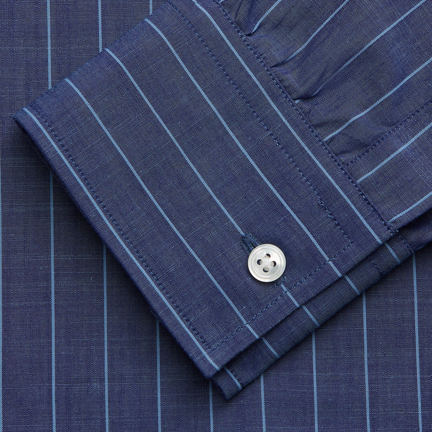 View 4 of product Close-up of a person wearing the Turnbull & Asser Blue Stripe Weekend Fit Nevis Shirt with Derby Collar and 1-Button Cuffs under a dark pinstripe blazer, focusing on the collar and upper chest. The face is partially out of frame.