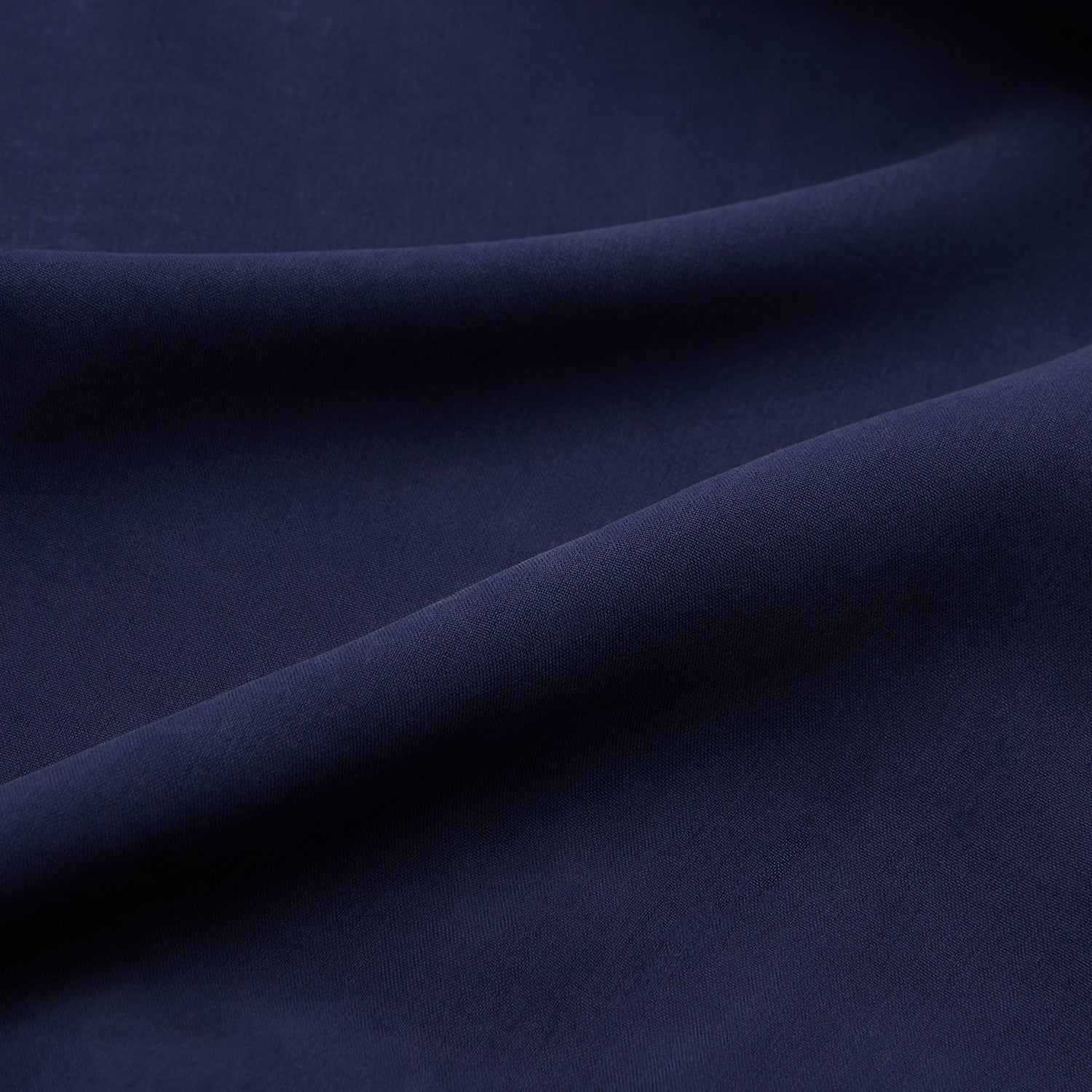 View 4 of product A man stands against a beige backdrop, wearing the Turnbull & Asser Navy Holiday Fit Silk Phillips Shirt with Revere Collar and dark pinstripe pants. He gazes downwards with a relaxed expression, embodying effortless summer style.