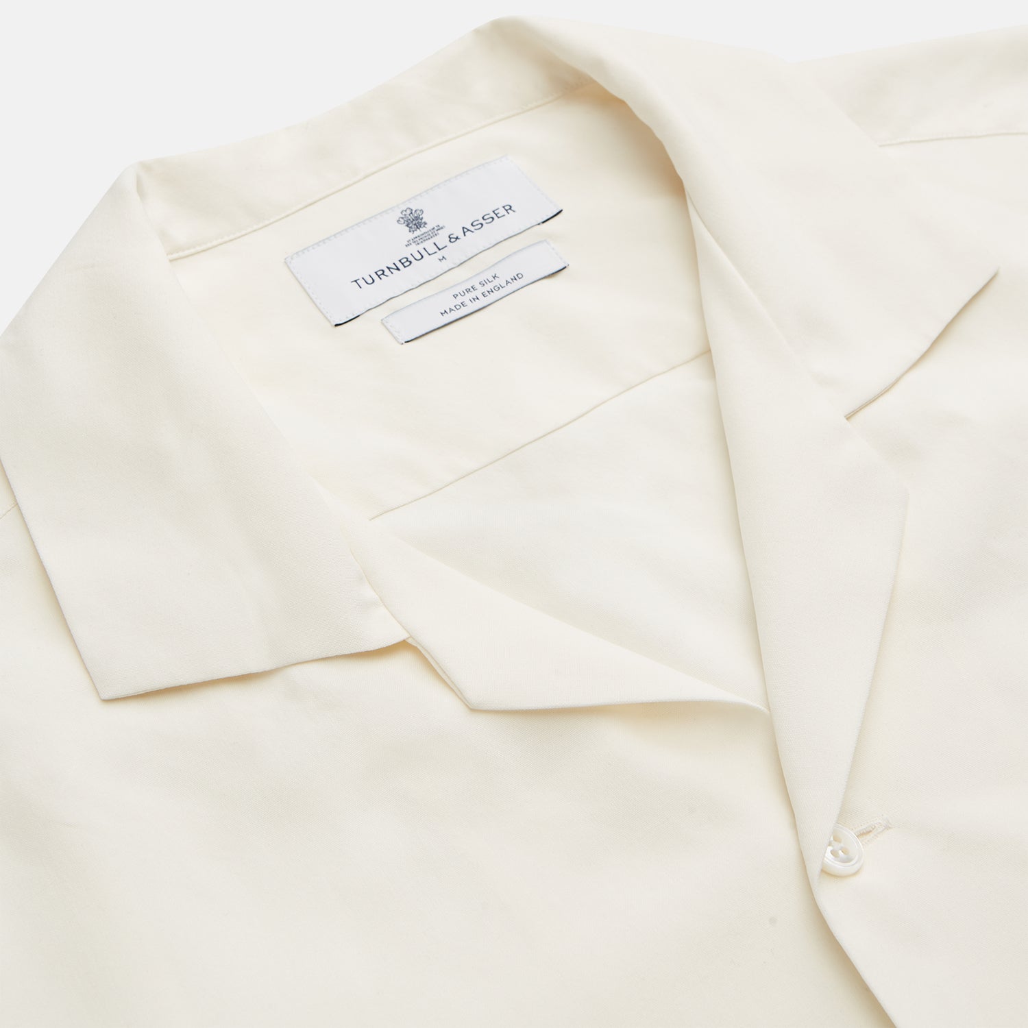 View 3 of product The Turnbull & Asser Cream Holiday Fit Silk Phillips Shirt features a revere collar, short sleeves, and three front pockets, shown flat on a white background.