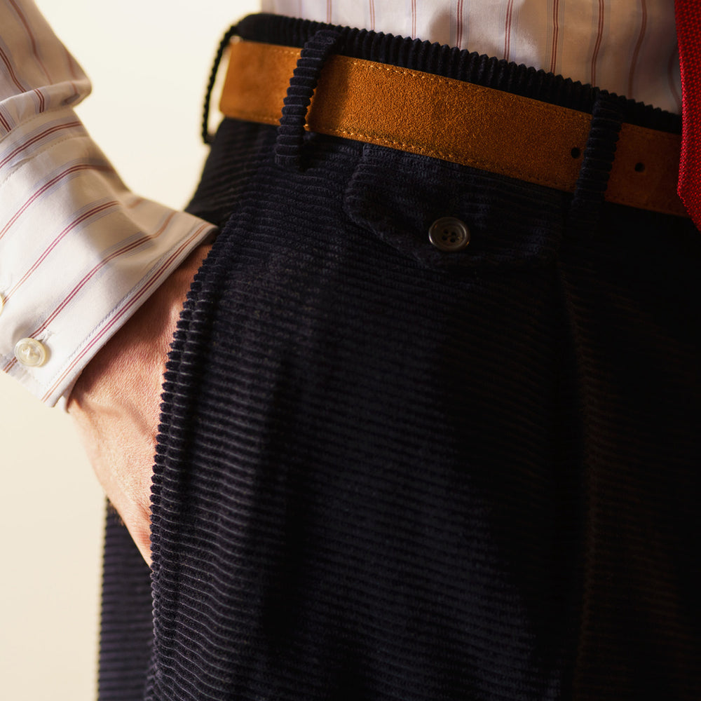 A pair of Turnbull & Asser Navy Horizontal Cord Nolan Trousers featuring a straight-leg fit, button and zip closure, front pleats, and classic horizontal cord texture, laid flat on a white background.