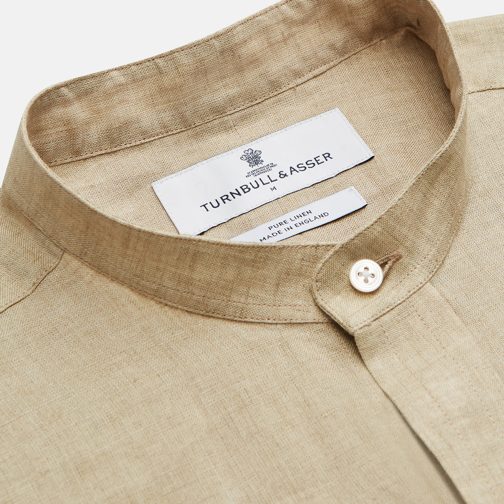 A man with a bald head and trimmed beard wears the Turnbull & Asser Beige Weekend Fit Linen Blake Shirt with stand collar and 1-button cuffs, standing calmly against a matching beige background.